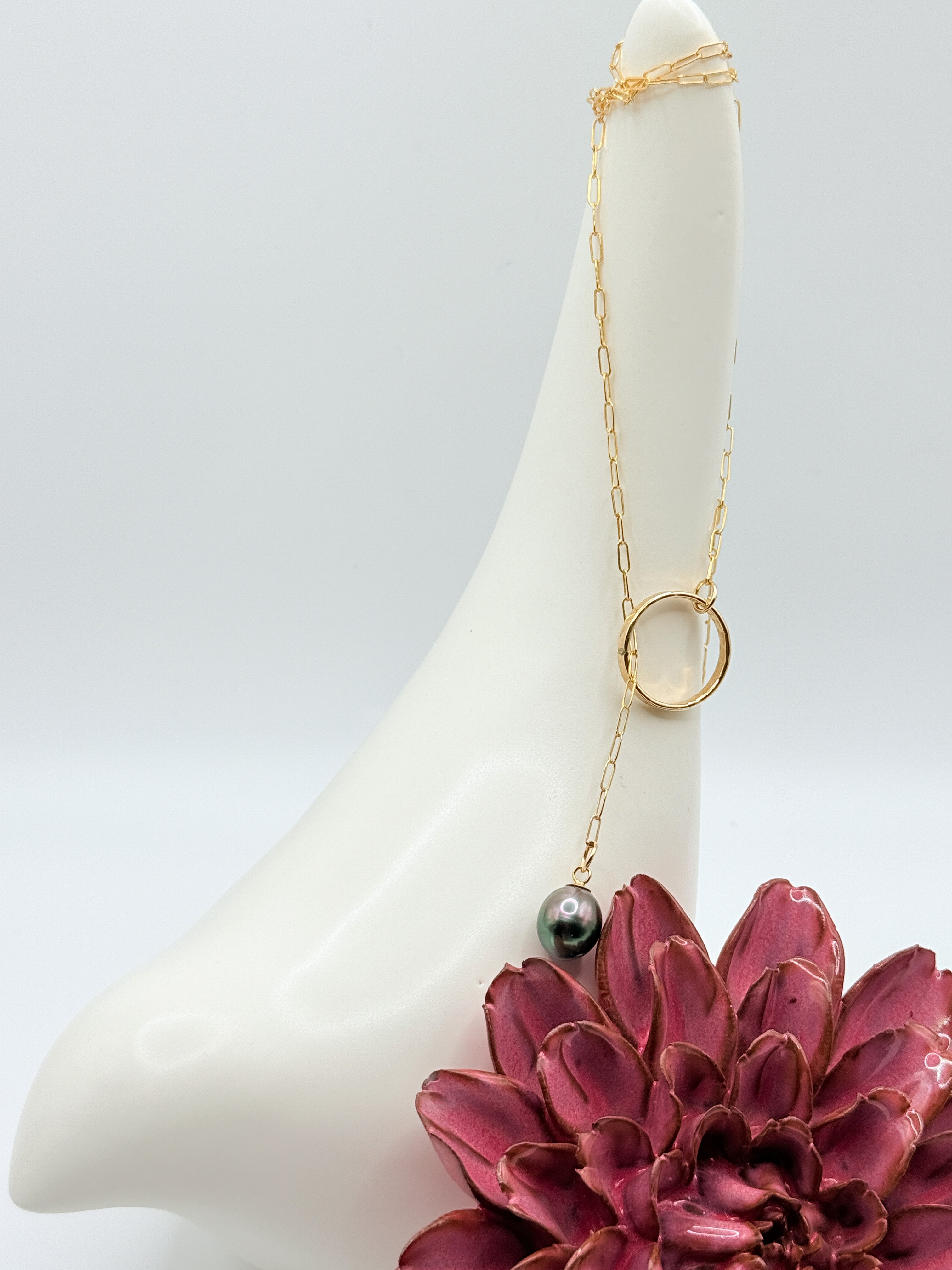 Gold chain lariat necklace with Tahitian pearl draped over white cone-shaped display stand with burgundy succulent, showing the adjustable lariat design