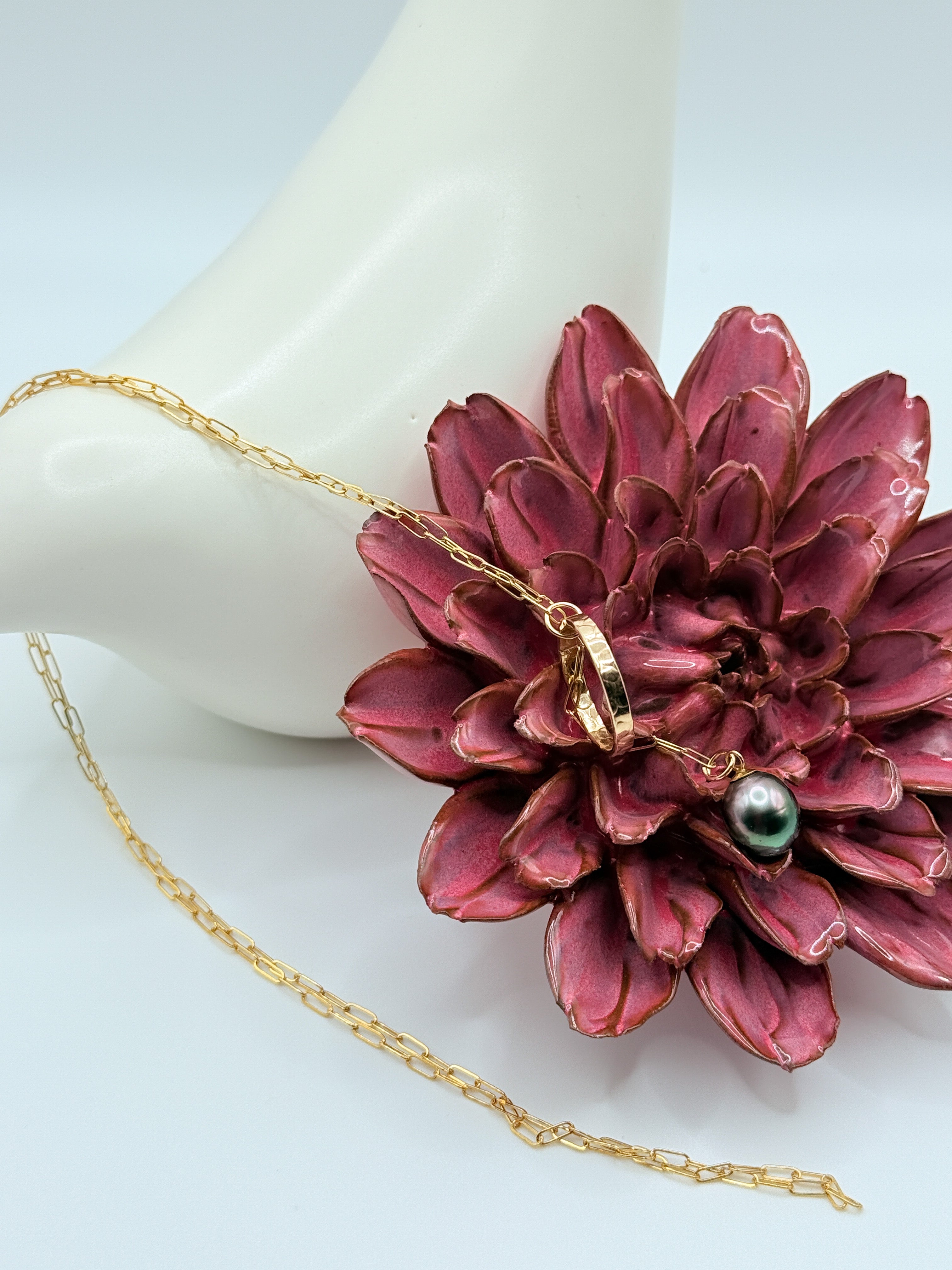 Gold chain lariat necklace with Tahitian pearl artistically styled with burgundy succulent flower against white ceramic bird, highlighting the warm gold tones