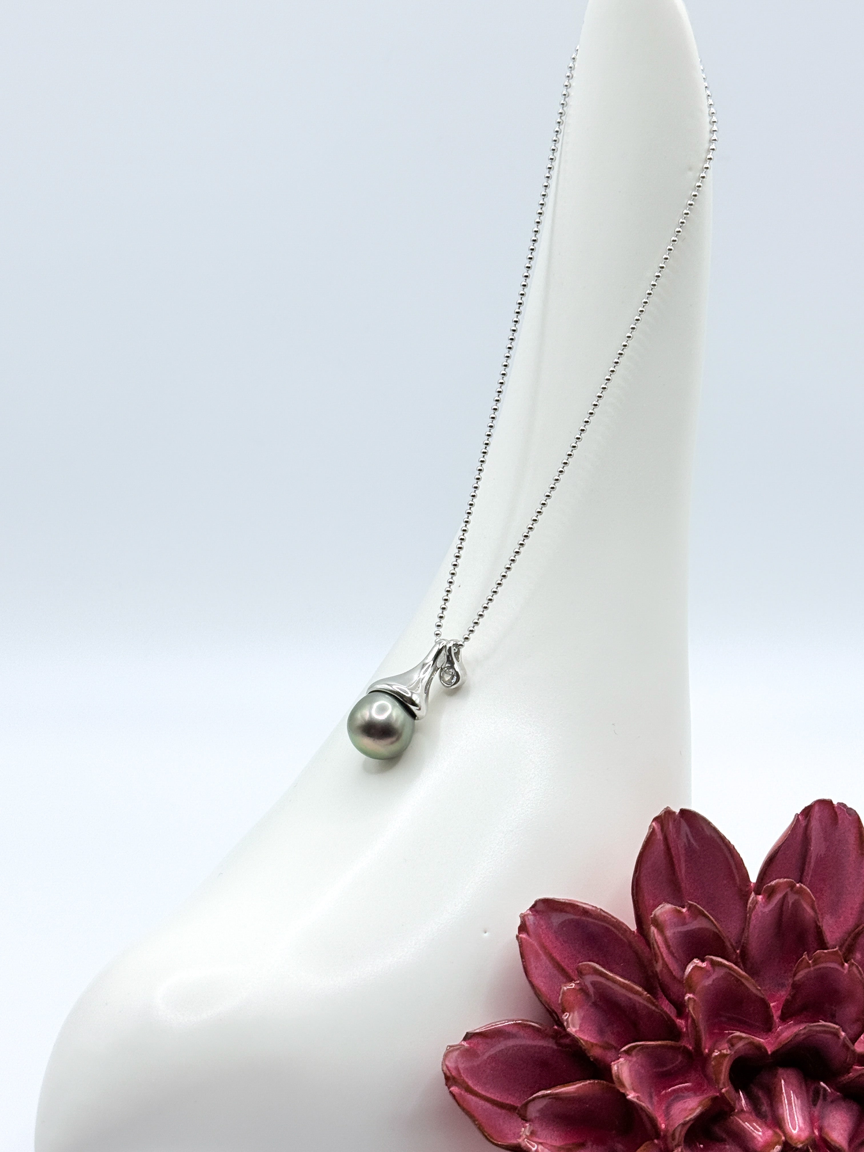 Sterling silver ball chain necklace with dark Tahitian pearl pendant in modern setting holder, styled with burgundy succulent and white ceramic bird