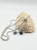 Sterling silver lariat necklace with two Tahitian pearls in different colours displayed on white coral specimen, showing one grey pearl and one dark green pearl with silver accents