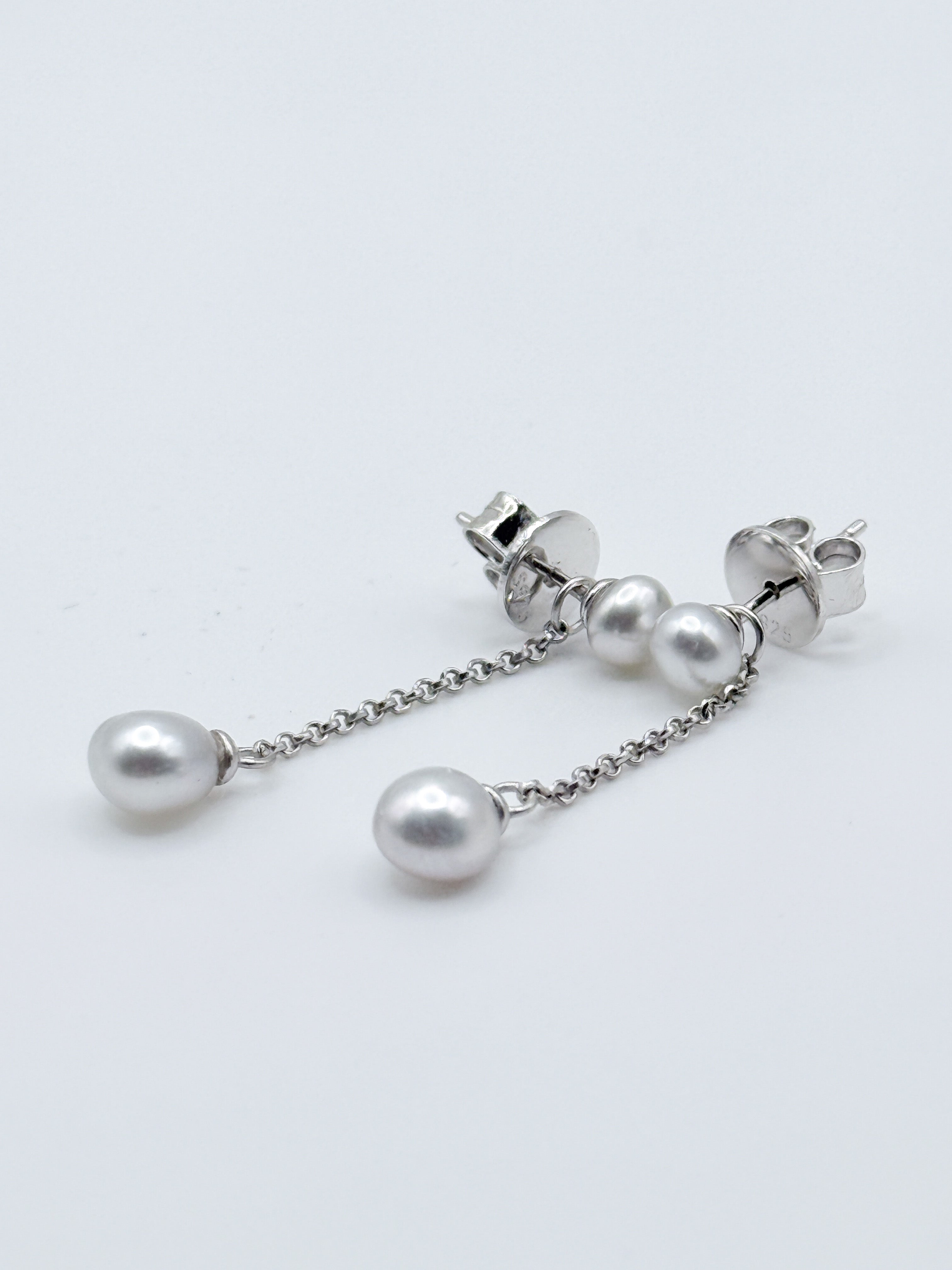 Close-up detail of sterling silver convertible earrings with white South Sea keshi pearls, showing the removable chain drops attached to stud backs on white background