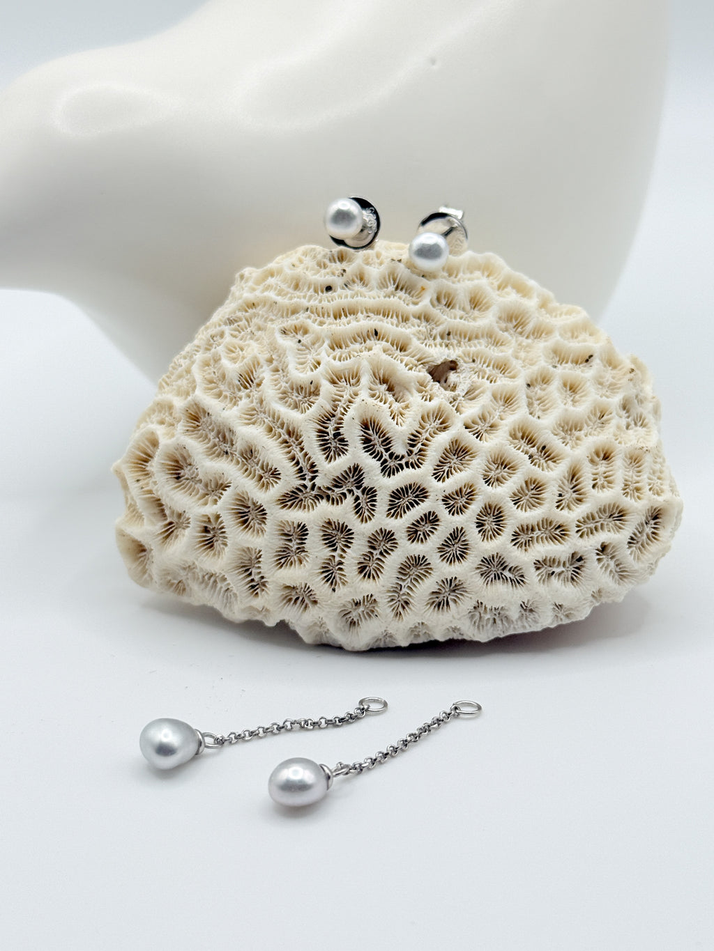 Sterling silver stud earrings with white South Sea keshi pearls and matching drop chain earrings displayed on white coral specimen