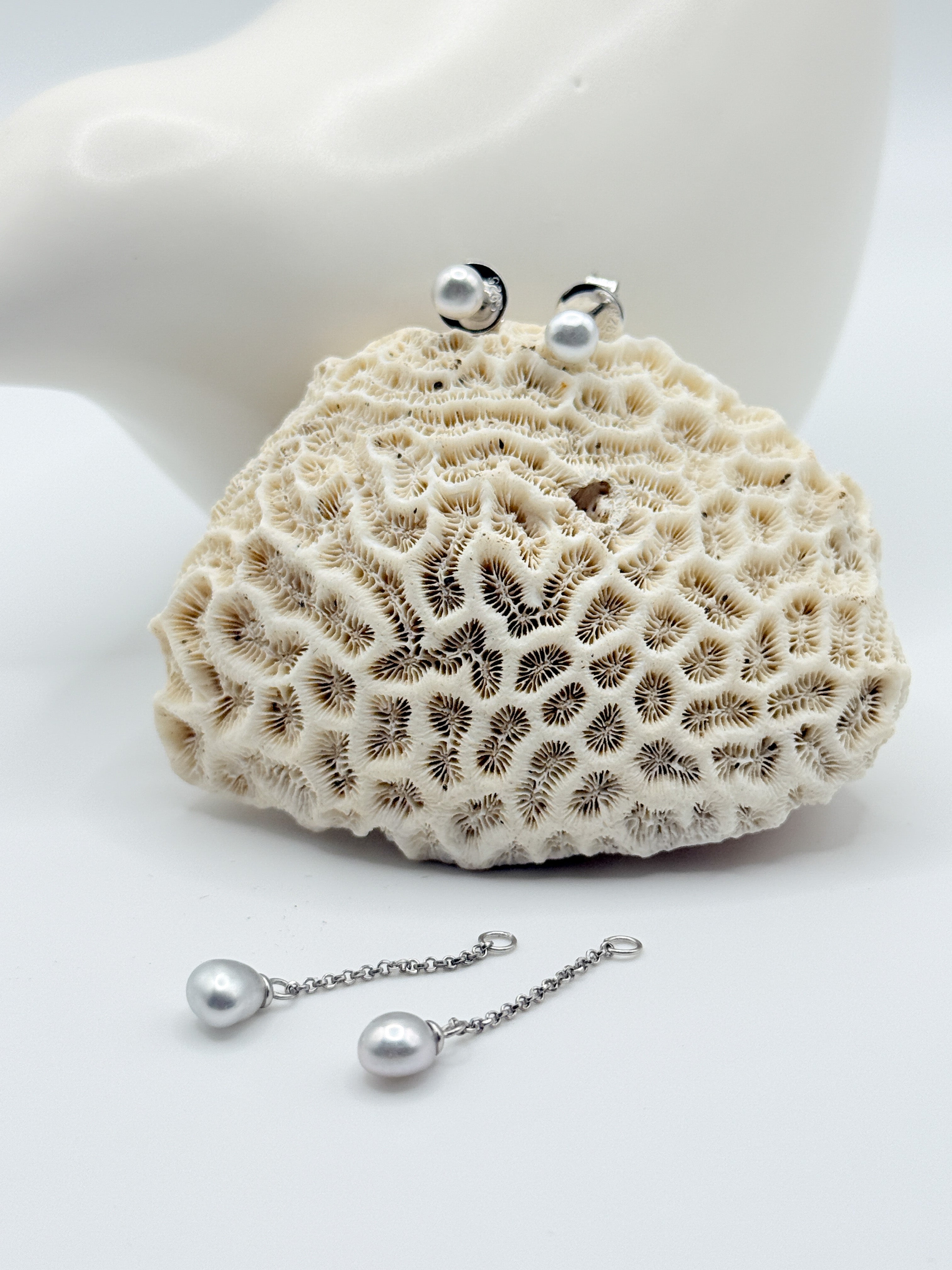 Sterling silver stud earrings with white South Sea keshi pearls and matching drop chain earrings displayed on white coral specimen