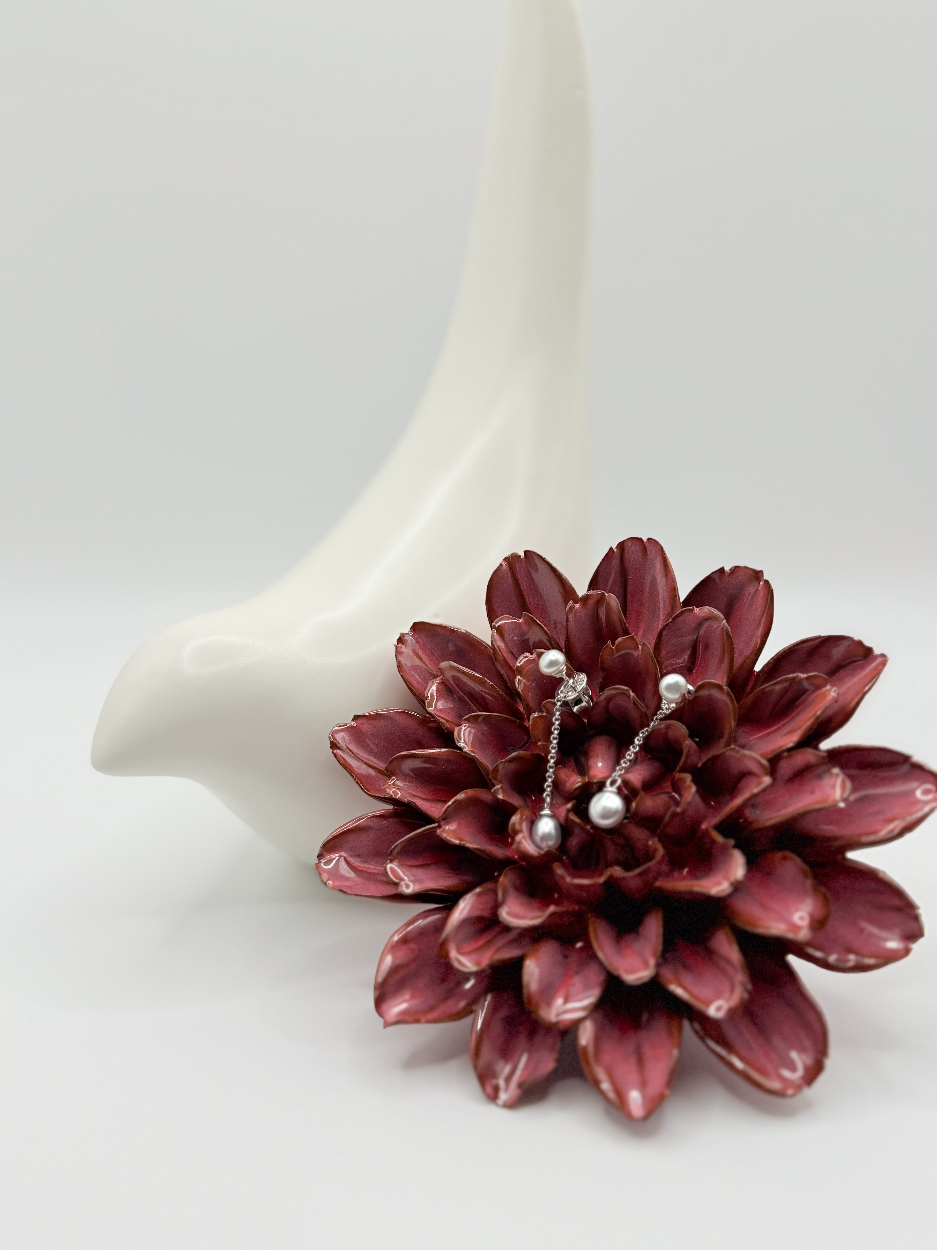 Sterling silver earrings with white South Sea keshi pearls nestled in burgundy succulent flower against white ceramic backdrop, showing the lustrous pearl surfaces