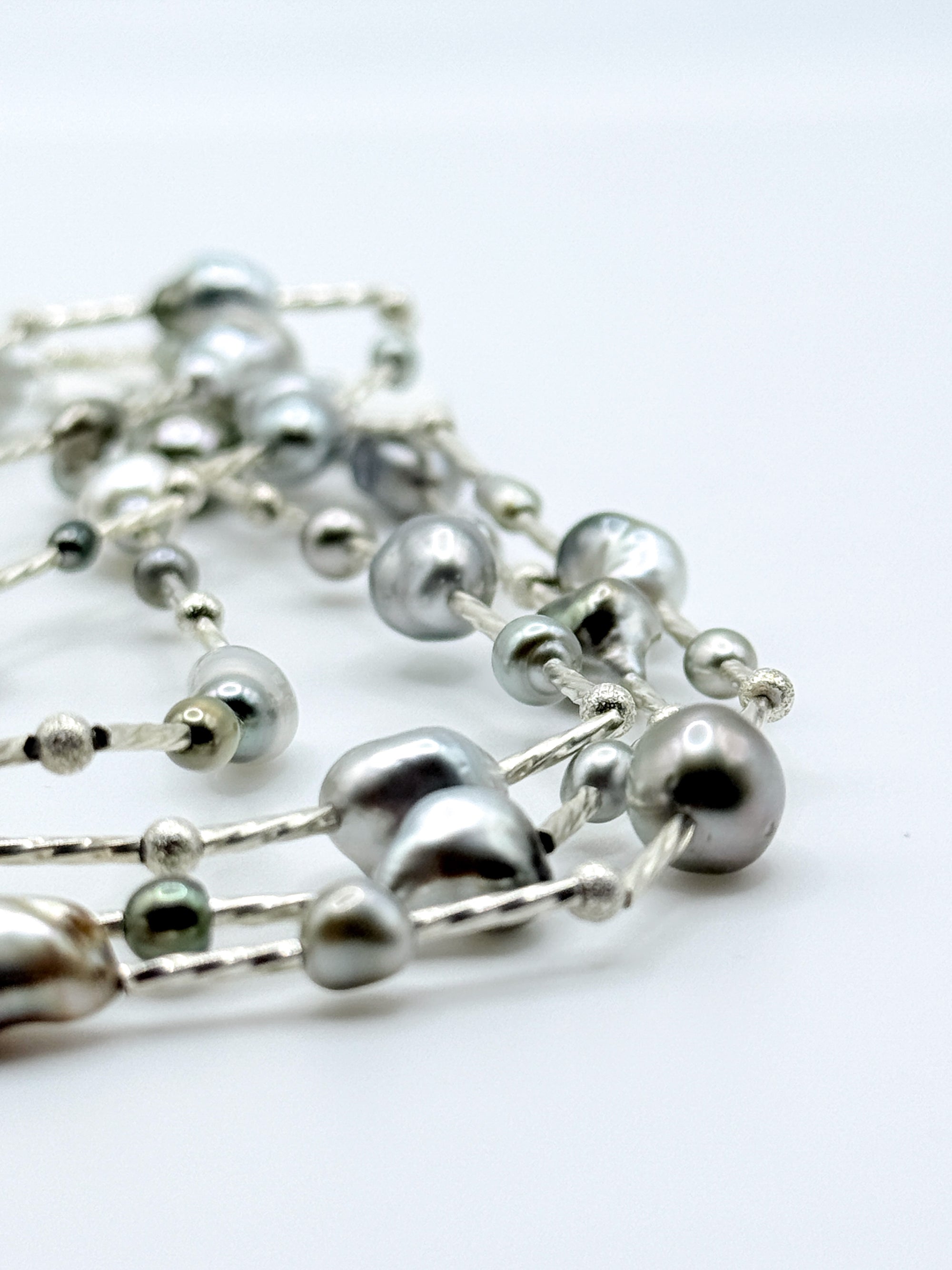 Close-up detail of sterling silver station necklace showing mixed Tahitian keshi pearls in various colours including silver, green, and peacock tones connected by delicate silver chain links