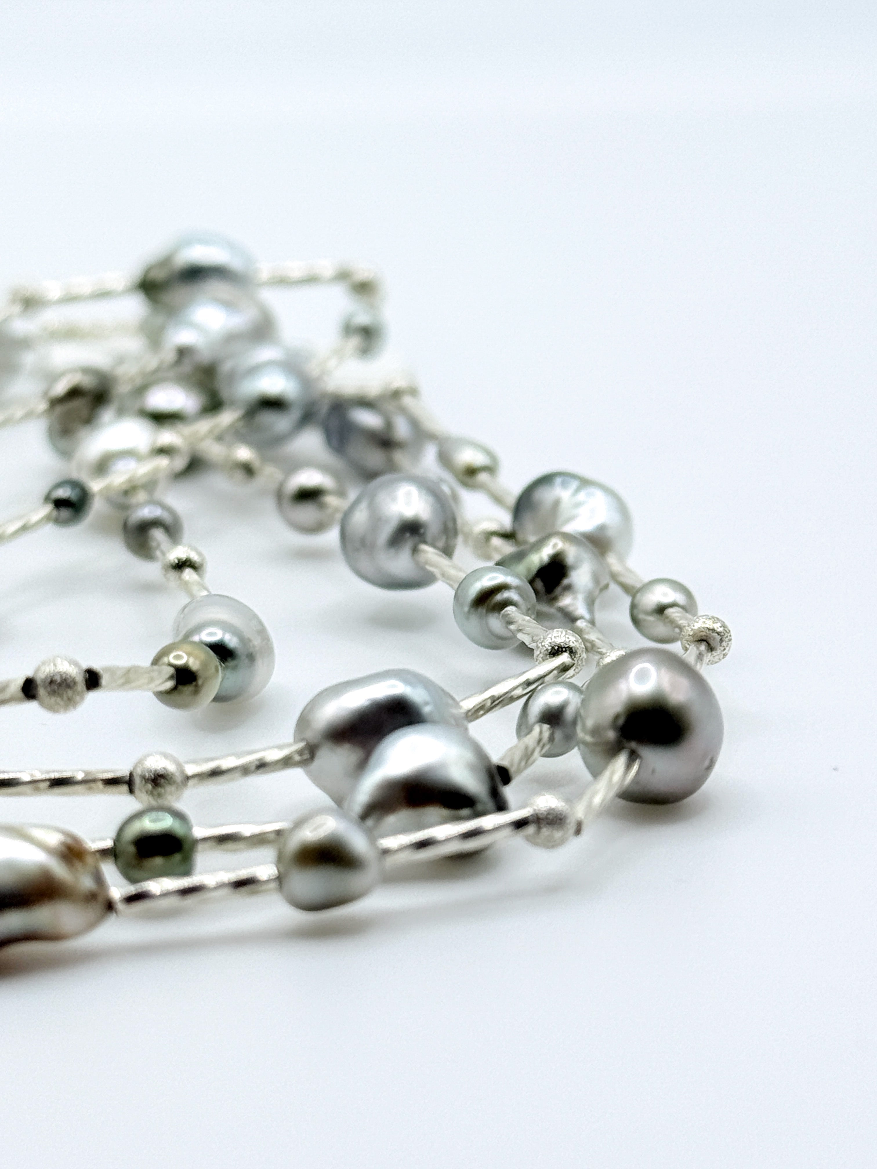 Close-up detail of sterling silver station necklace showing mixed Tahitian keshi pearls in various colours including silver, green, and peacock tones connected by delicate silver chain links