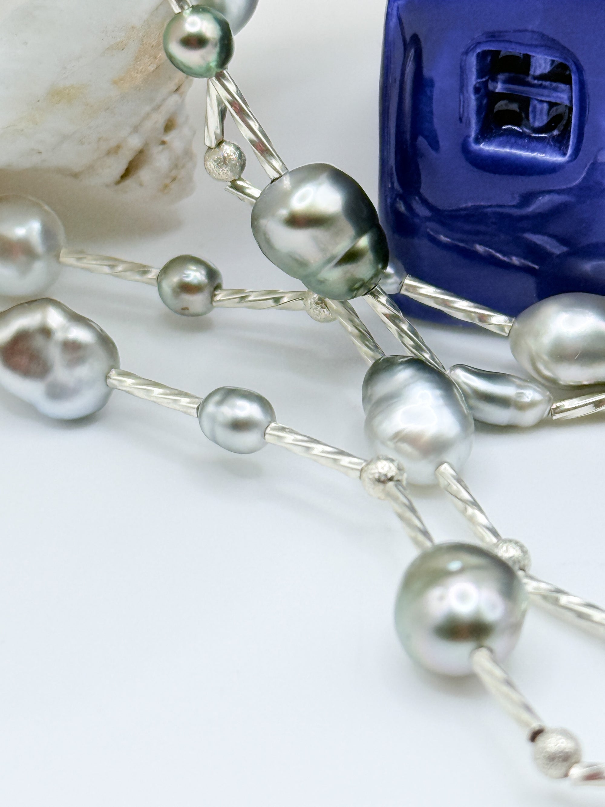 Macro close-up of sterling silver station necklace showing individual Tahitian keshi pearls with beautiful green and silver overtones connected by delicate silver chain links and decorative silver beads