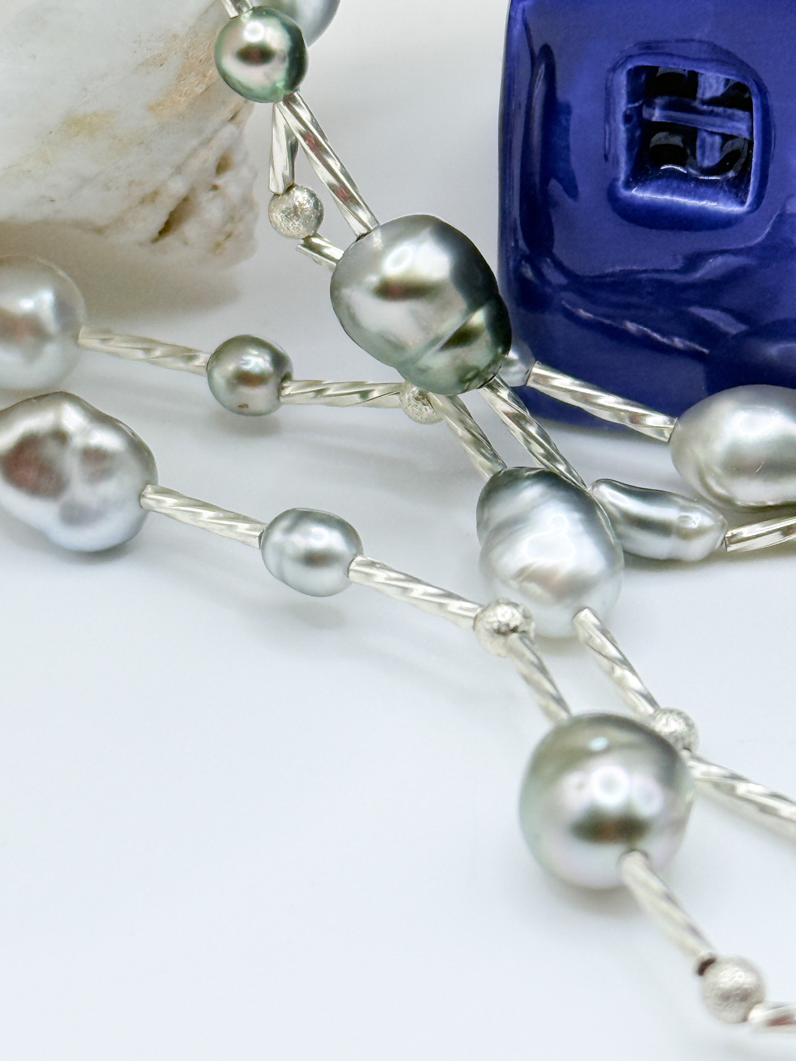 Macro close-up of sterling silver station necklace showing individual Tahitian keshi pearls with beautiful green and silver overtones connected by delicate silver chain links and decorative silver beads