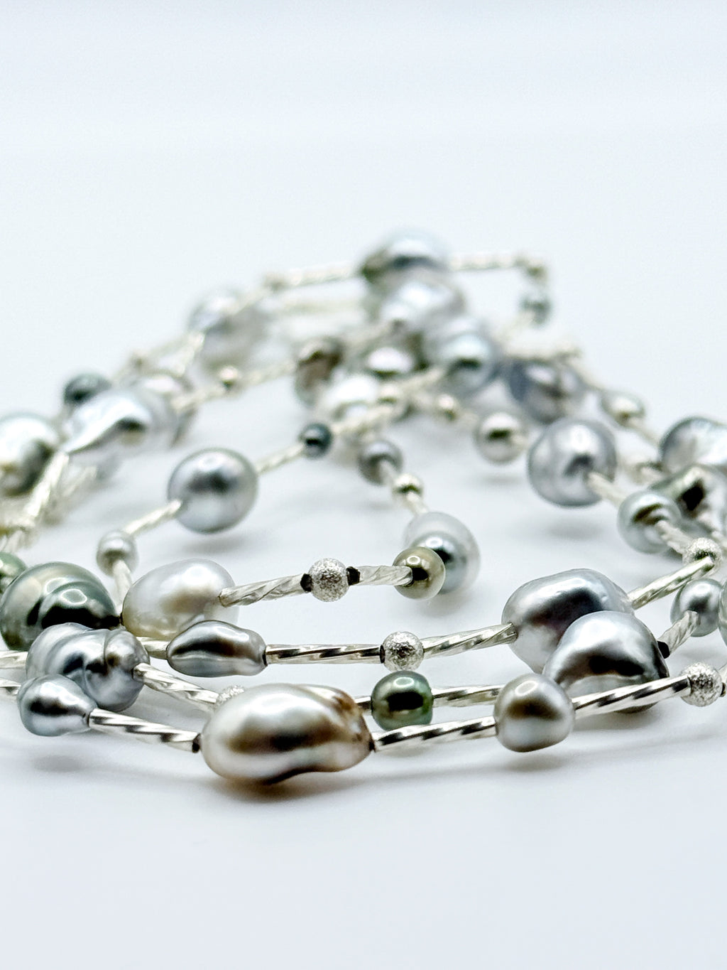 Artistic close-up of sterling silver station necklace with Tahitian keshi pearls in soft focus, highlighting the lustrous surfaces and organic baroque shapes of the pearls