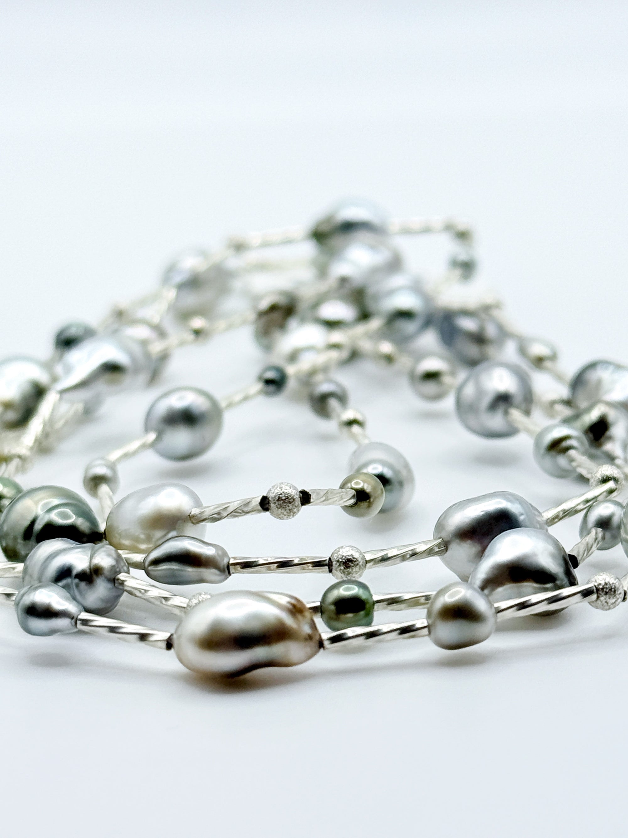 Artistic close-up of sterling silver station necklace with Tahitian keshi pearls in soft focus, highlighting the lustrous surfaces and organic baroque shapes of the pearls