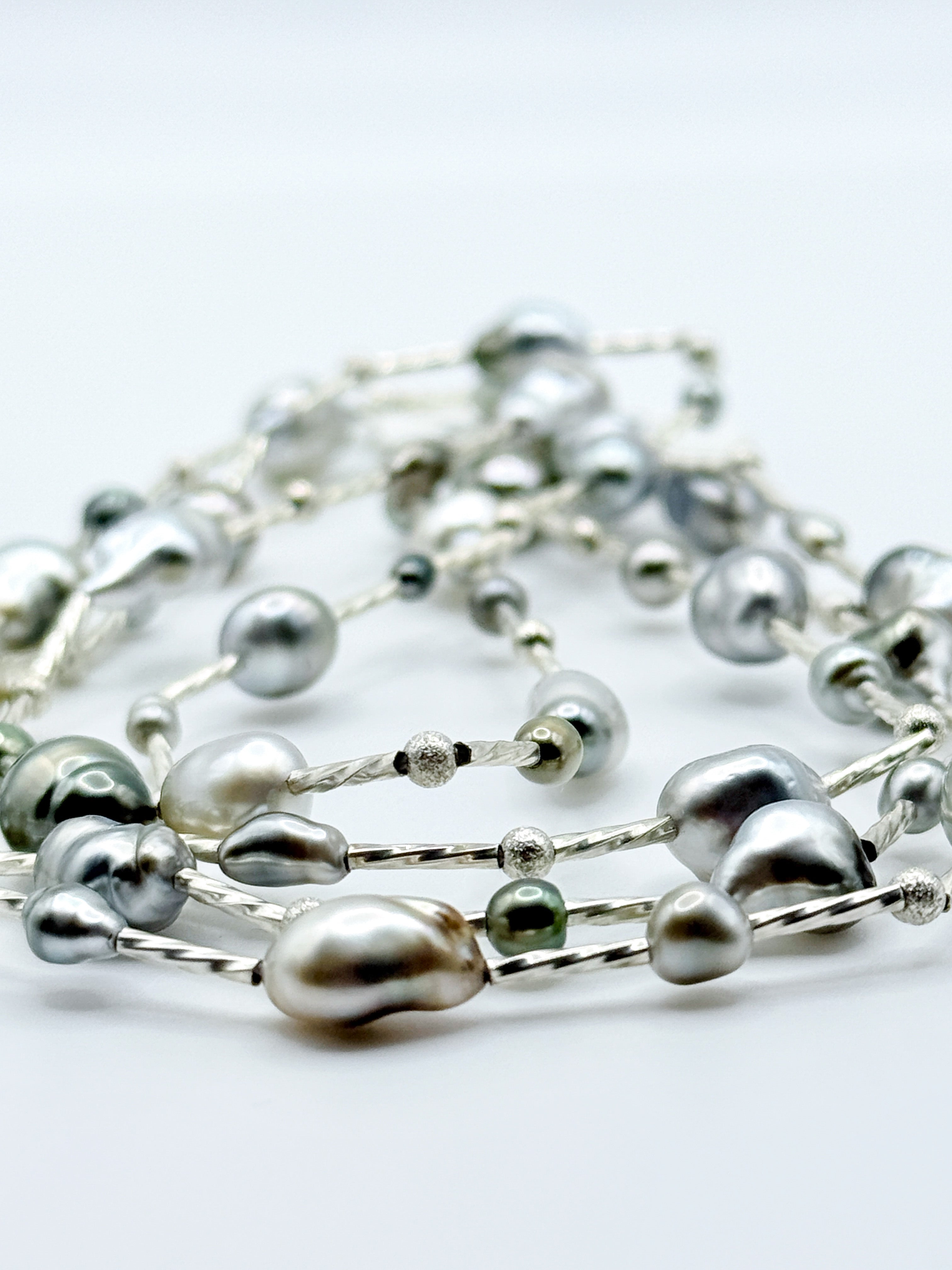 Artistic close-up of sterling silver station necklace with Tahitian keshi pearls in soft focus, highlighting the lustrous surfaces and organic baroque shapes of the pearls