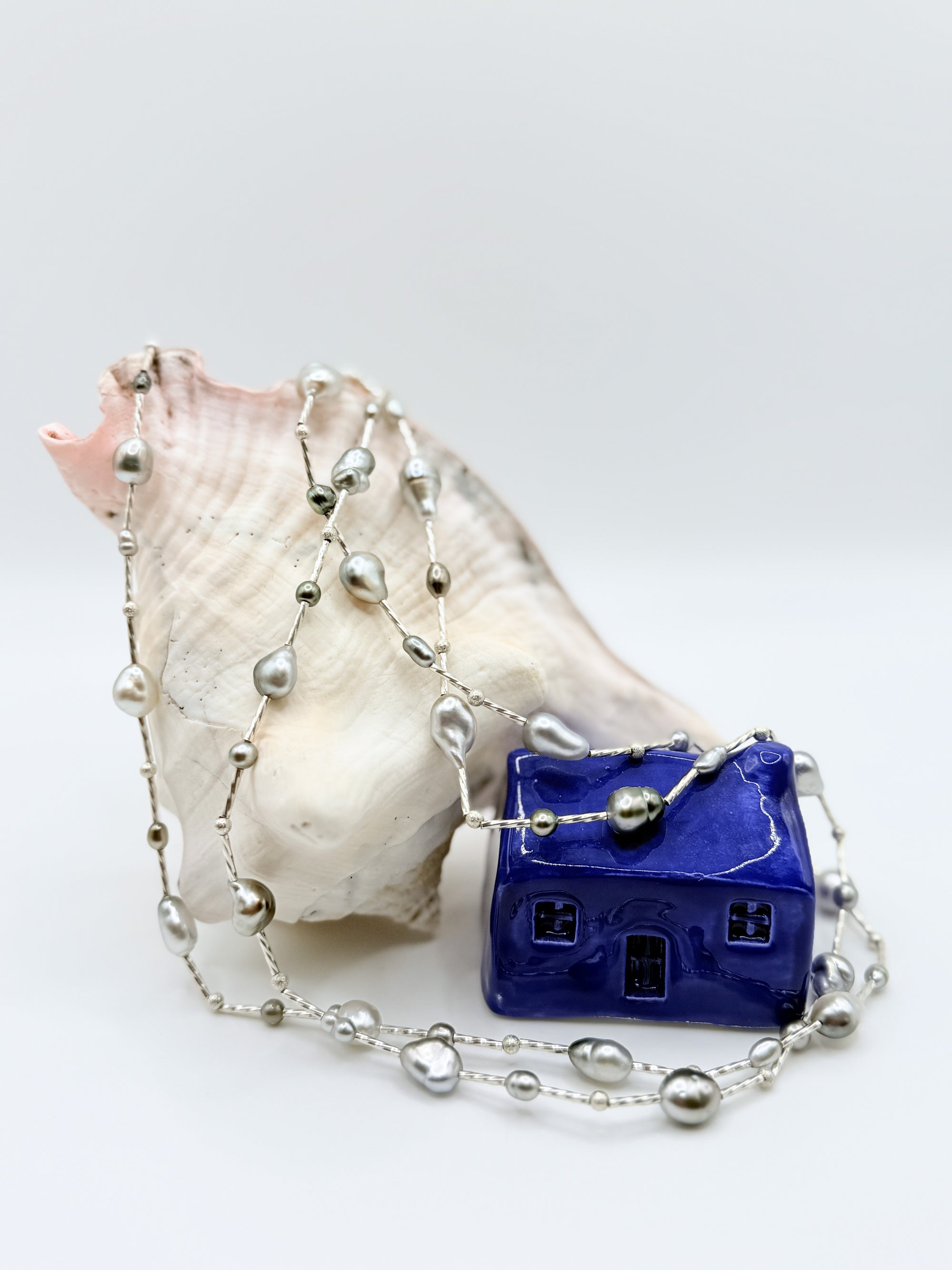 Sterling silver station necklace with mixed Tahitian keshi pearls cascading over white conch shell, displaying the variety of pearl shapes and colours from silver to peacock green