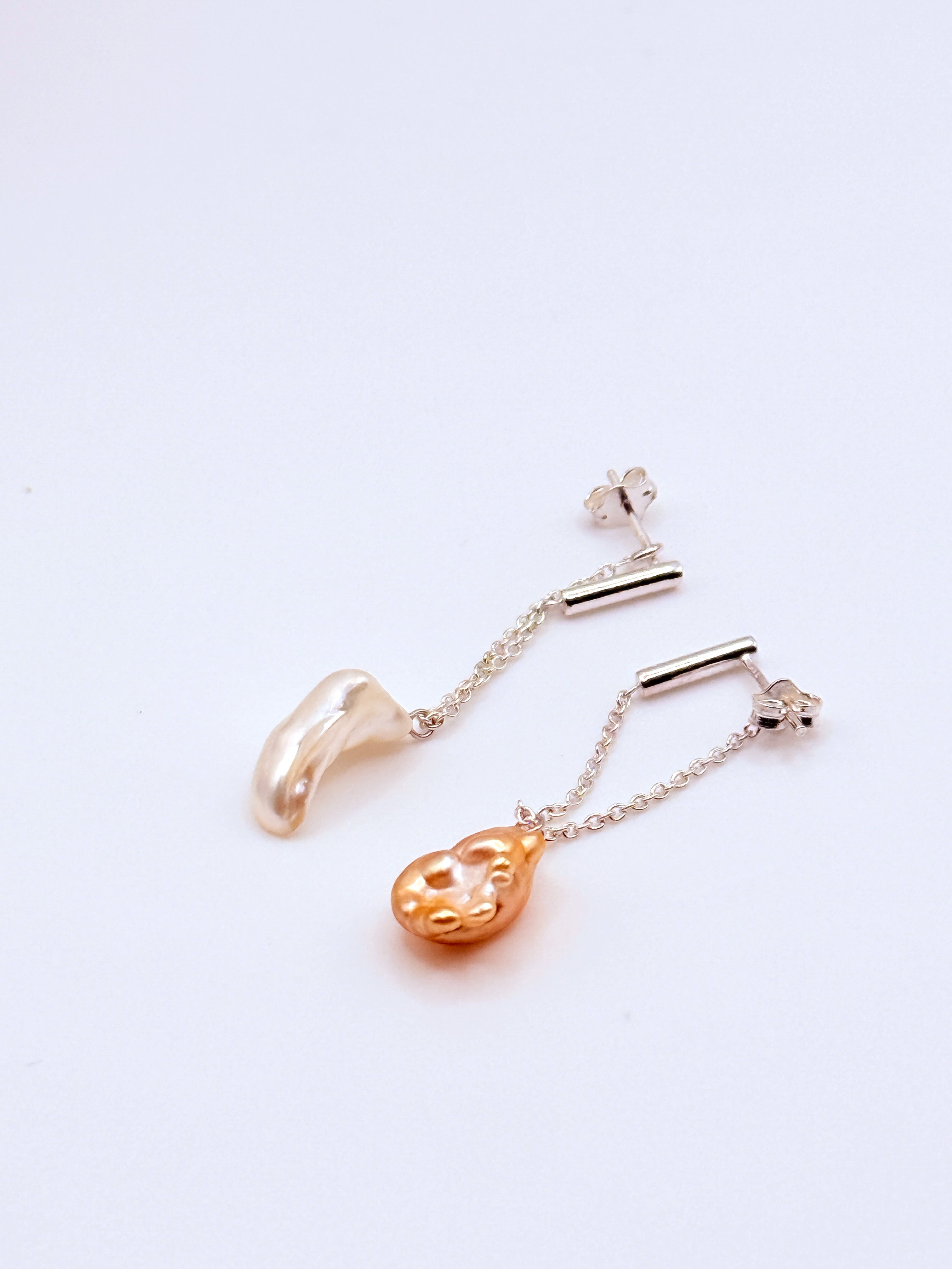 Asymmetrical gold drop earrings with South Sea keshi pearls laid flat on white background, showing the contrasting white and golden baroque pearl shapes