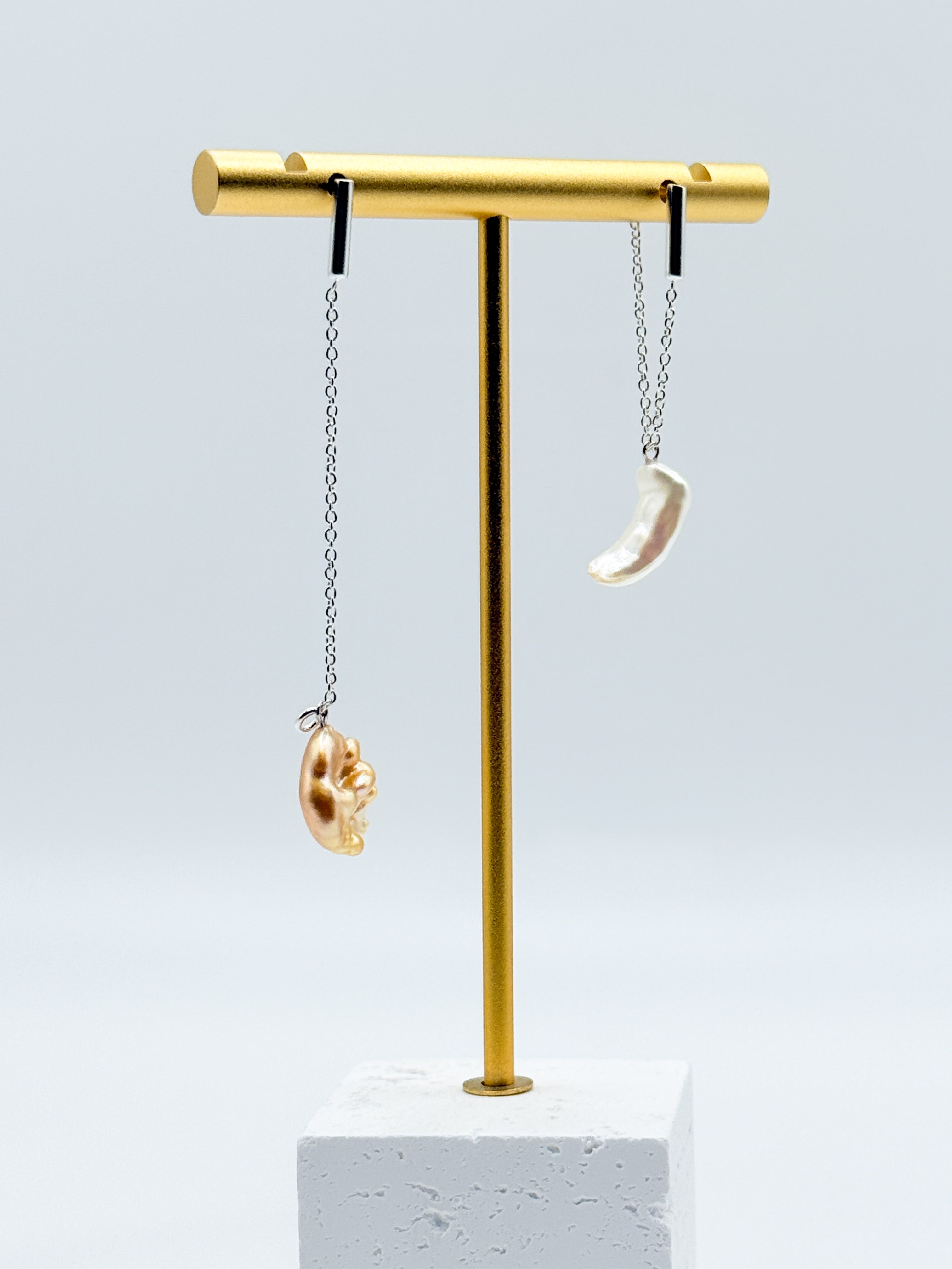 Asymmetrical gold drop earrings with white and golden South Sea keshi pearls displayed on gold jewellery stand, showing mismatched design with different pearl colours front view