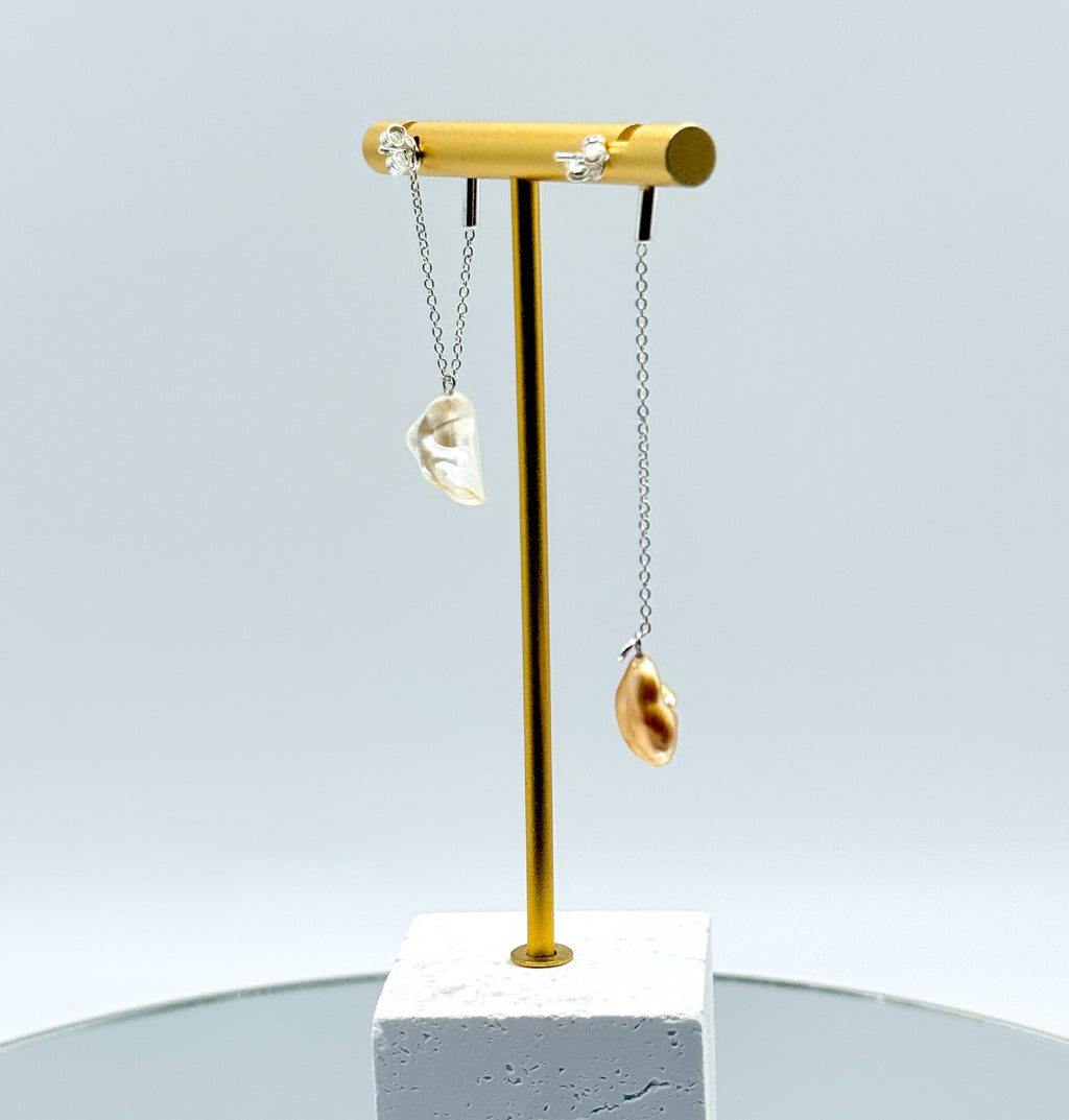 Gold chain drop earrings with asymmetrical South Sea keshi pearls on gold display stand, featuring one white pearl and one golden pearl on delicate chains back view