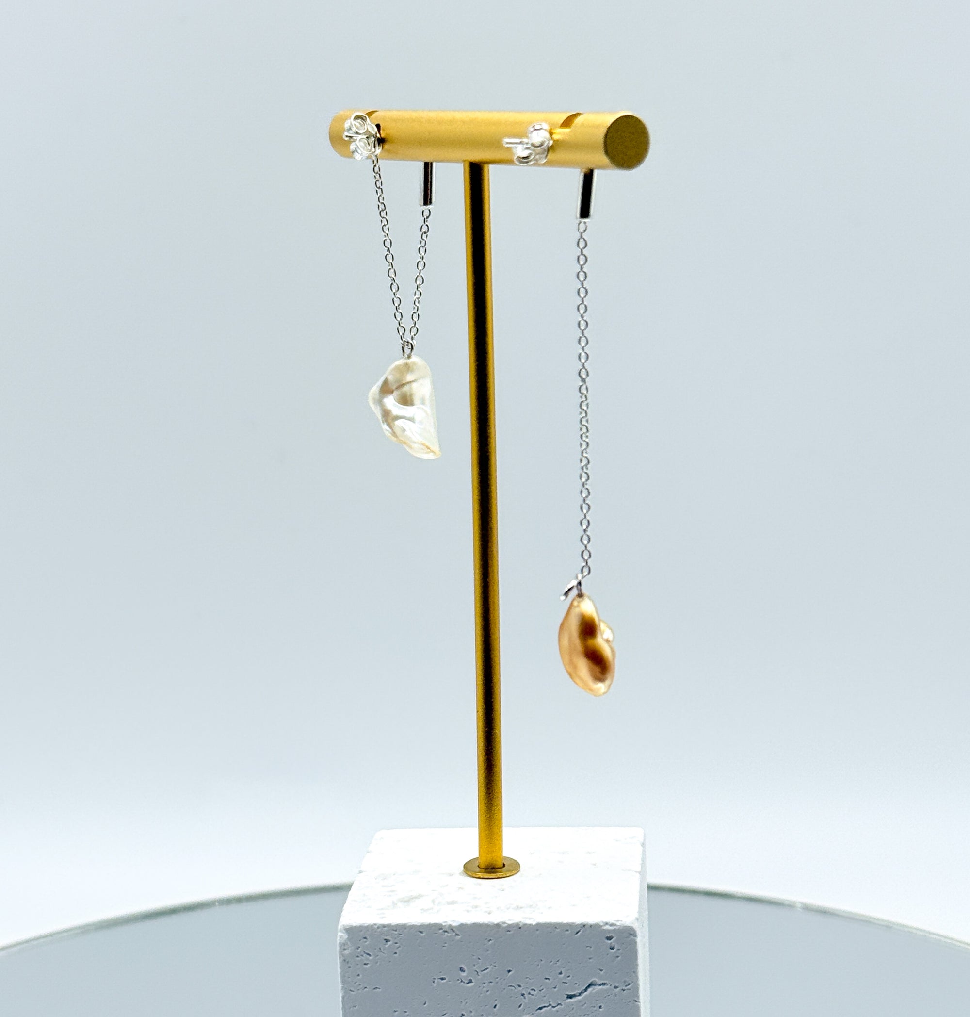 Gold chain drop earrings with asymmetrical South Sea keshi pearls on gold display stand, featuring one white pearl and one golden pearl on delicate chains back view