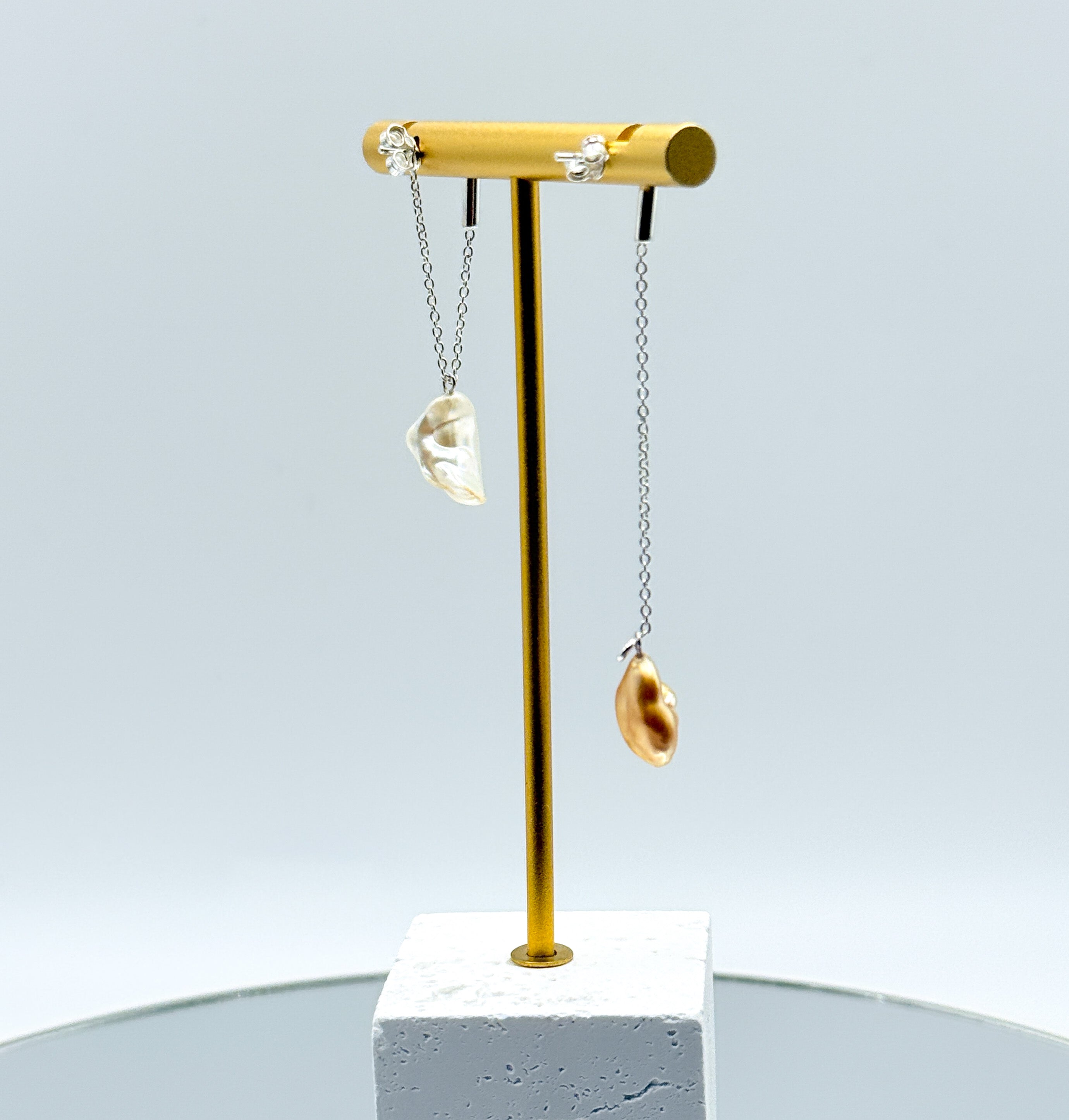 Gold chain drop earrings with asymmetrical South Sea keshi pearls on gold display stand, featuring one white pearl and one golden pearl on delicate chains back view