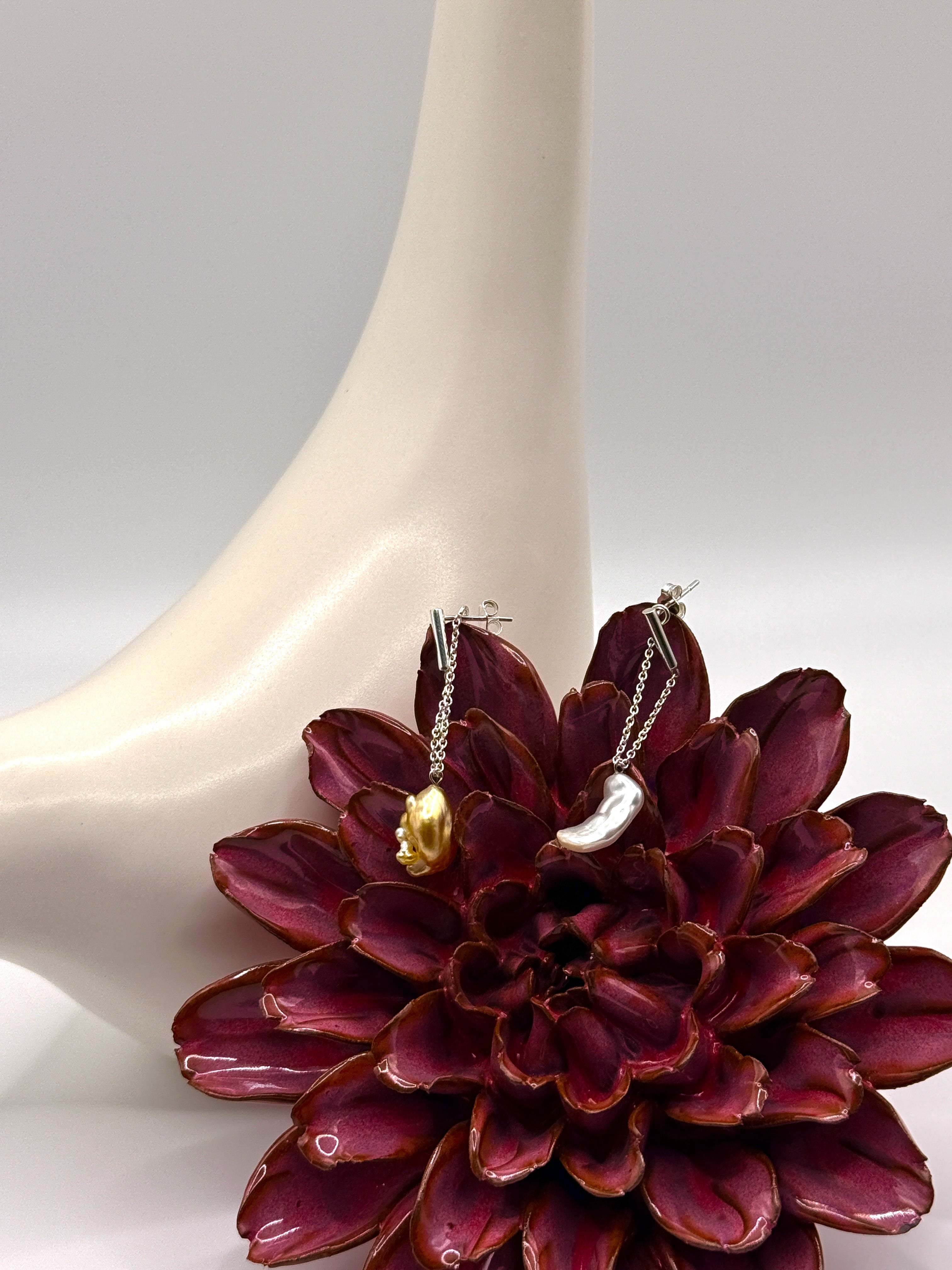 Asymmetrical gold drop earrings with South Sea keshi pearls nestled in burgundy succulent flower against white ceramic bird, highlighting the contrast between white and golden pearls