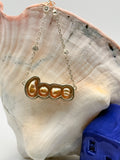 Close-up of gold 'LOVE' pendant necklace with golden South Sea keshi pearls on conch shell, highlighting the individual letter in pendant case connected by delicate silver chain with Spectacle set CZ 