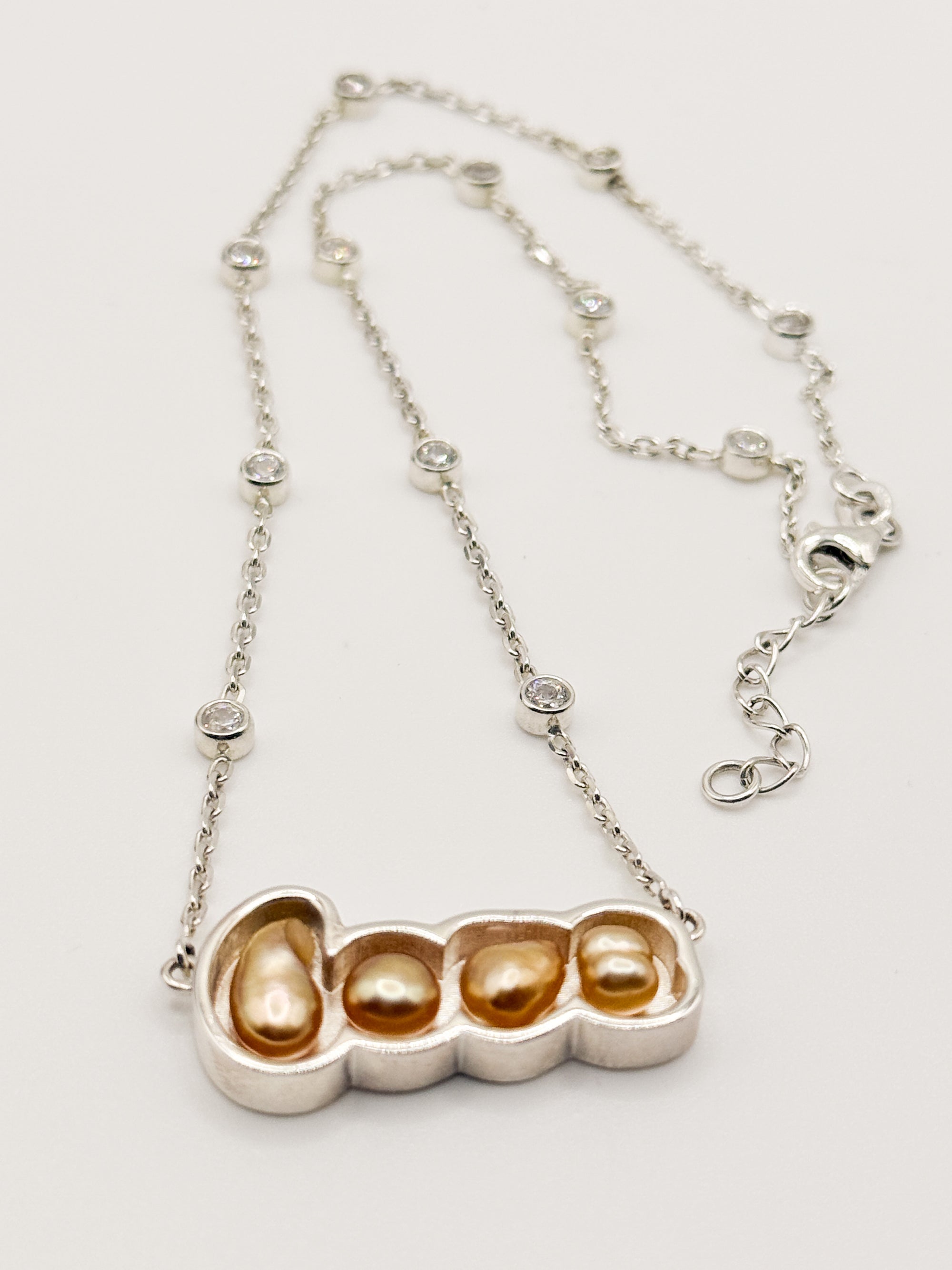 Detailed flat lay of gold 'LOVE' pendant necklace with golden South Sea keshi pearls on white background, displaying the CZ-studded chain and pendant construction