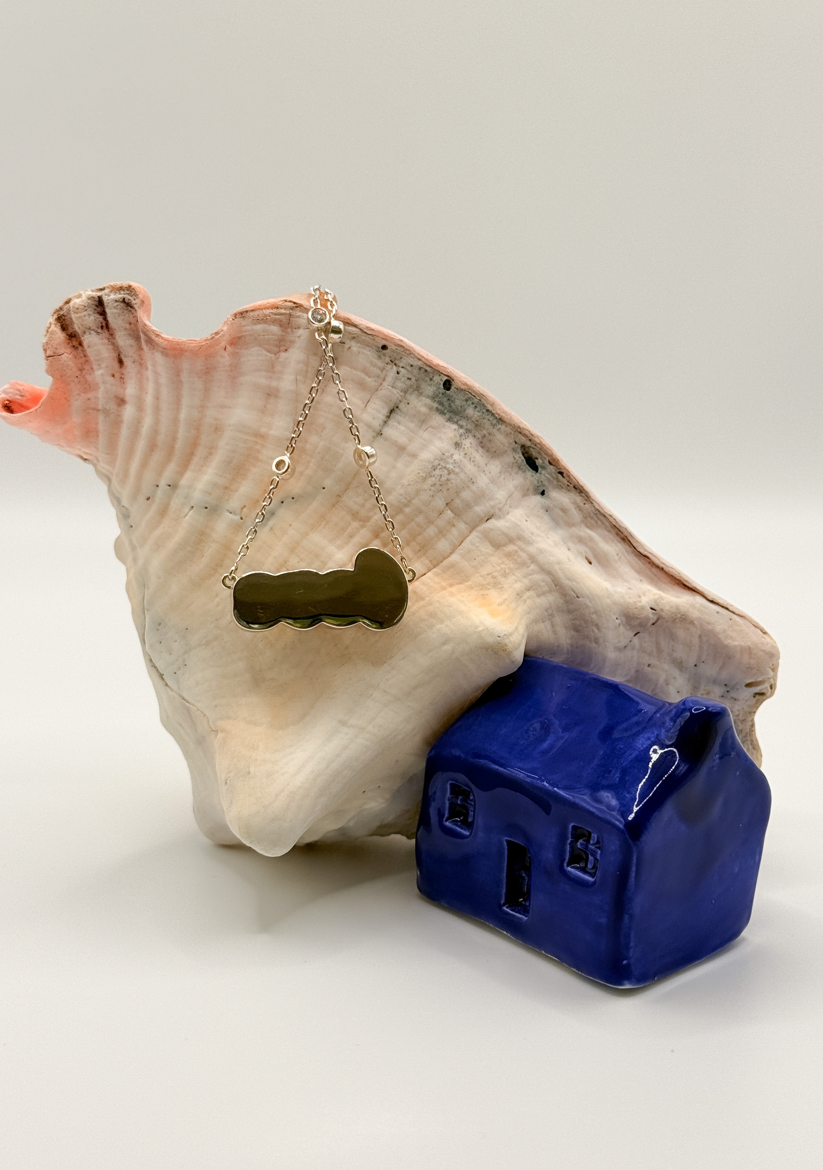 Gold 'LOVE' pendant necklace with South Sea keshi pearls hanging gracefully on large conch shell, showcasing the close back mounting of the pendant