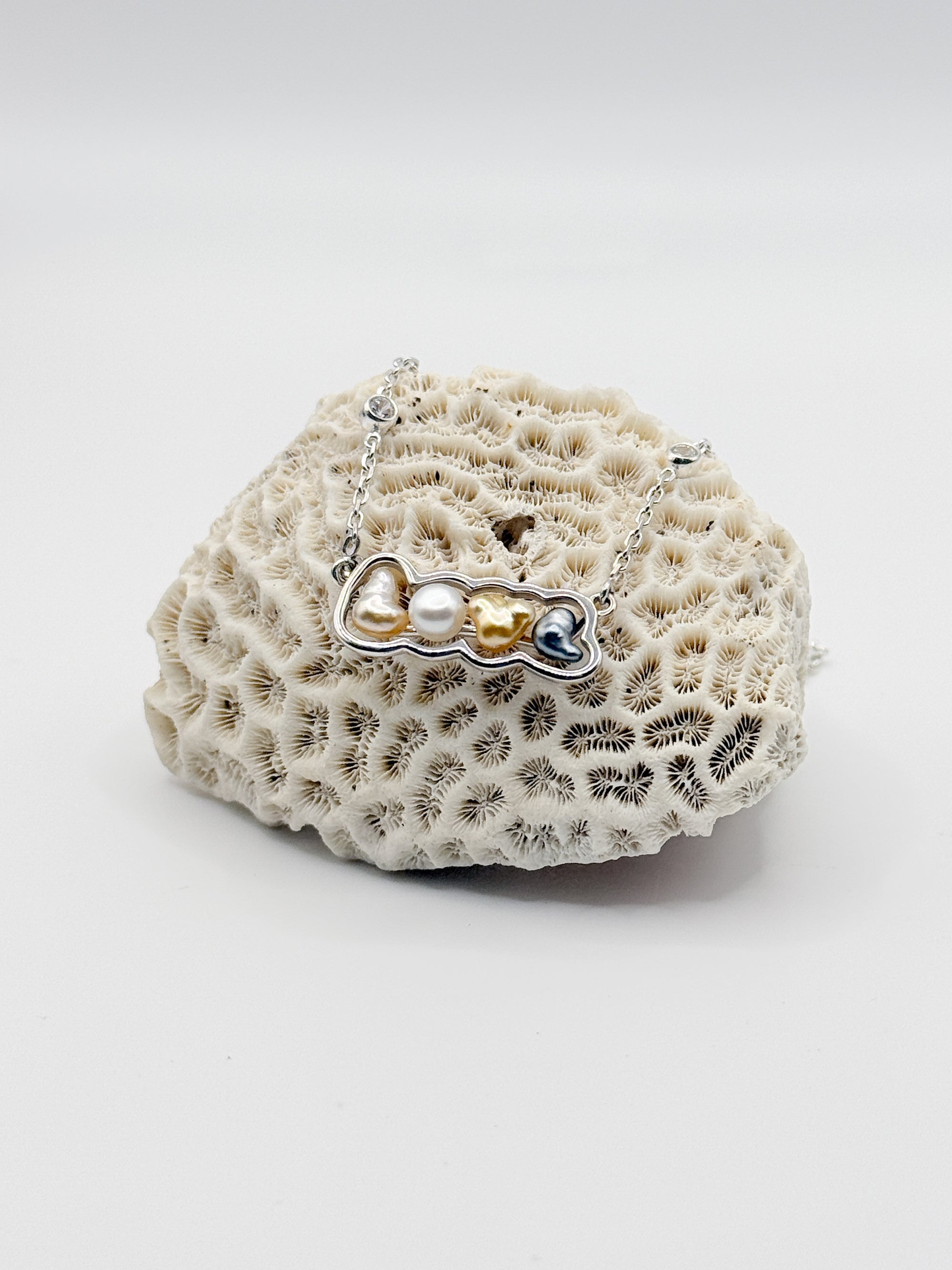 Sterling silver 'LOVE' pendant necklace with multi-coloured keshi pearls displayed on white coral specimen, showing the variety of pearl colours spelling out the word