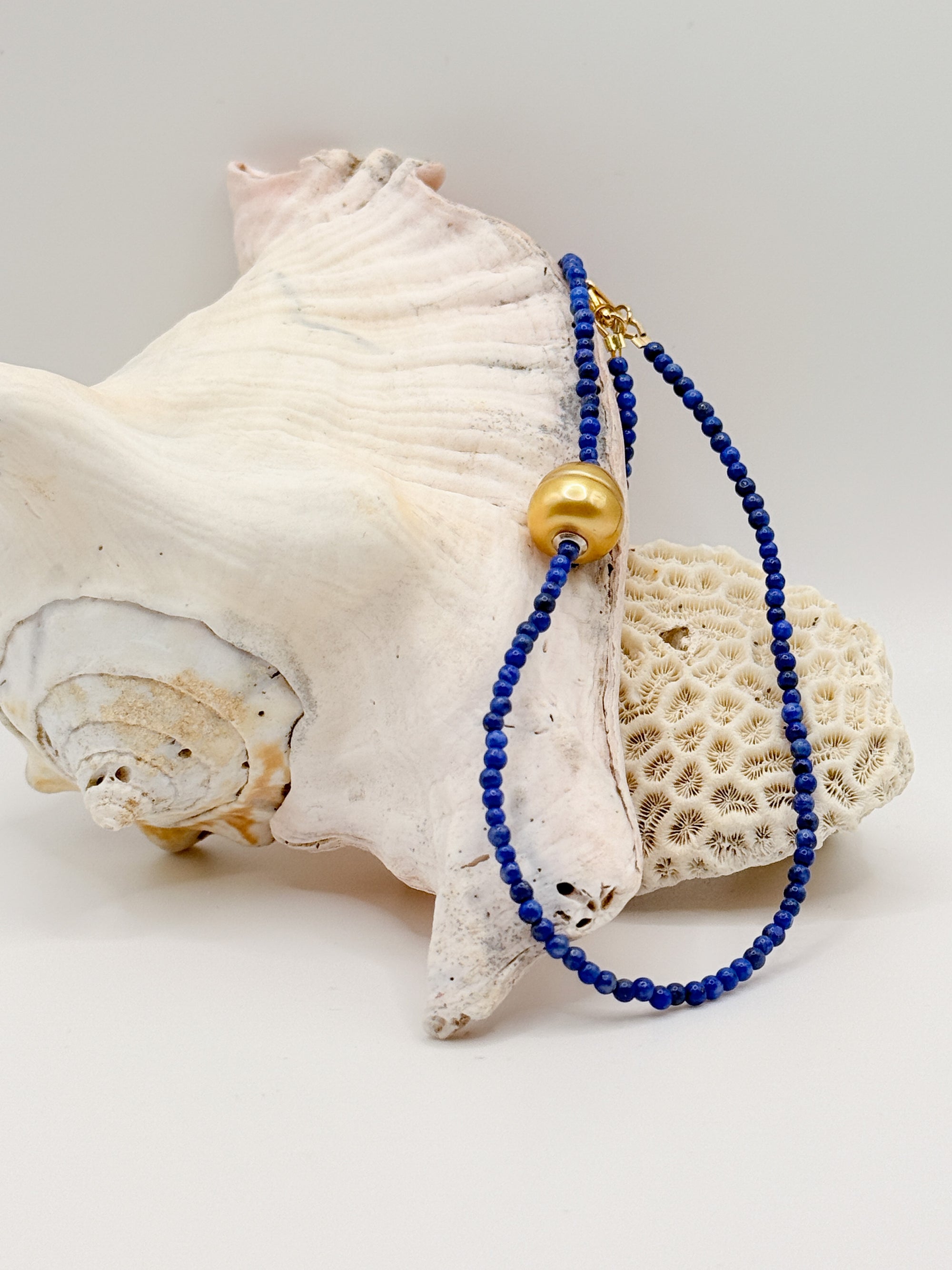 Close-up of golden South Sea pearl choker with lapis lazuli beads displayed on white coral and shell specimens, highlighting the rich blue gemstone texture and golden pearl lustre
