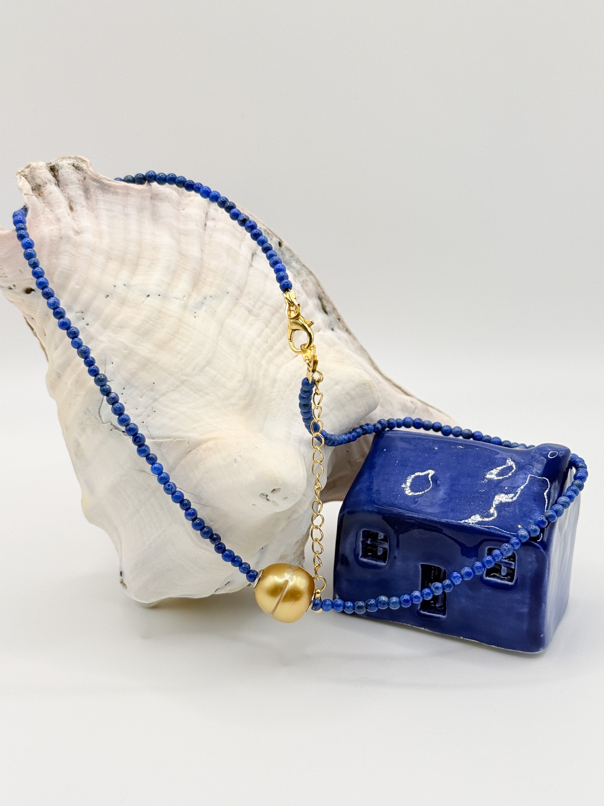 Golden South Sea pearl choker with lapis lazuli beads gracefully draped over large white conch shell and coral specimen, showing the gold clasp and extension chain details