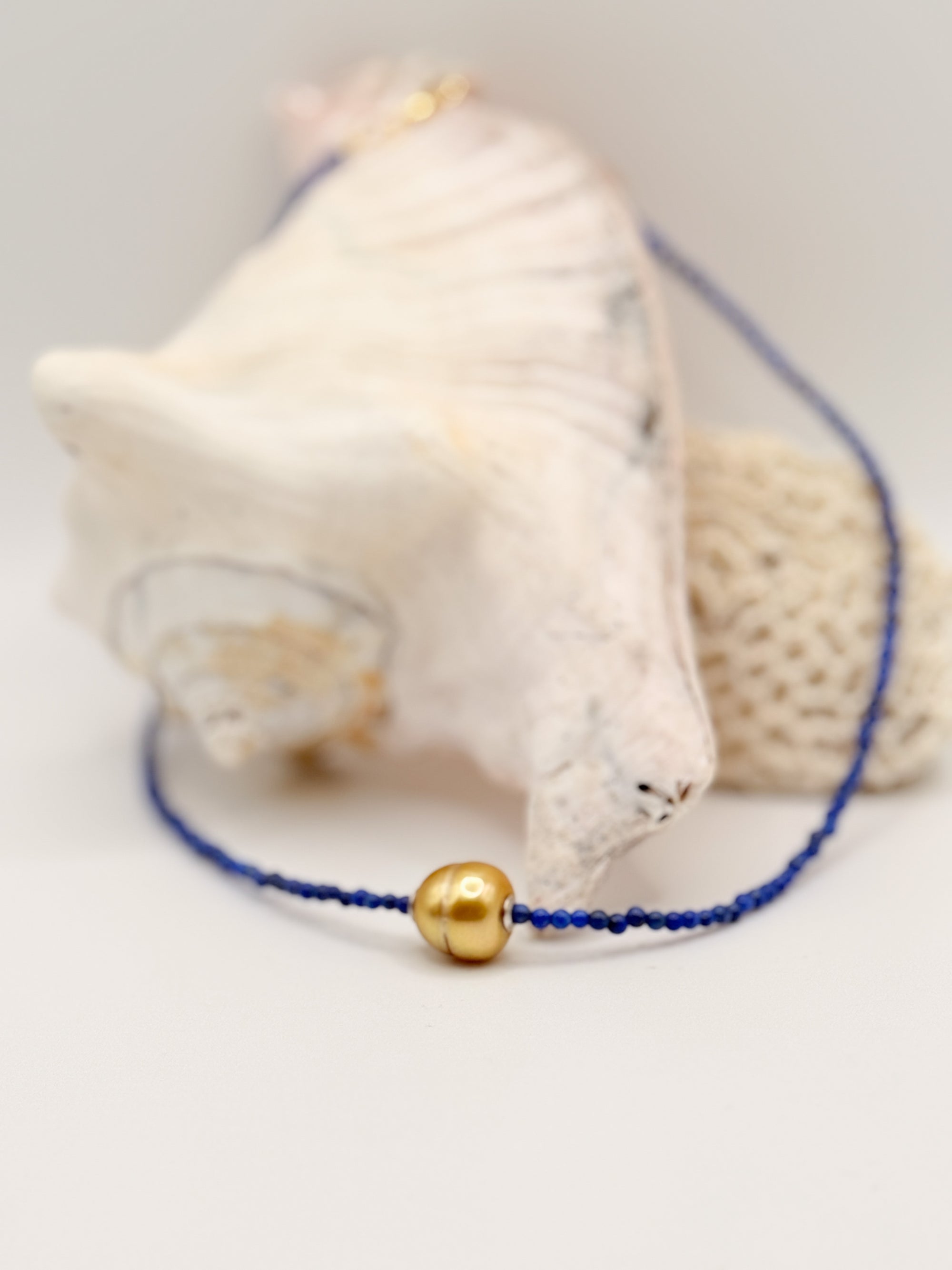 Close-up of golden South Sea pearl choker with lapis lazuli beads displayed on white coral and shell specimens, highlighting the rich blue gemstone texture and golden pearl lustre