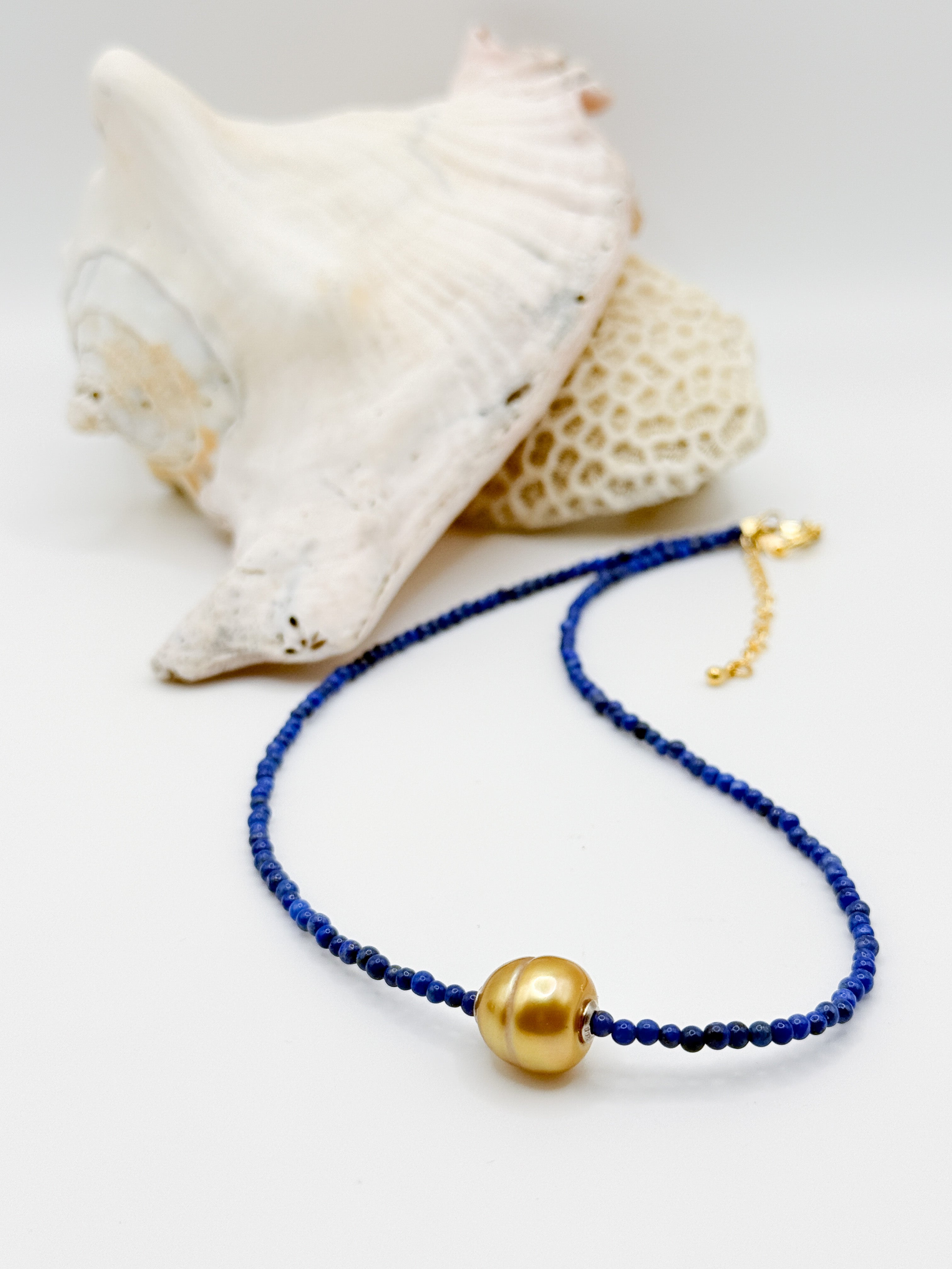 Golden South Sea pearl choker with lapis lazuli beads laid in curved formation next to white coral specimen, showcasing the contrast between deep blue beads and lustrous golden pearl