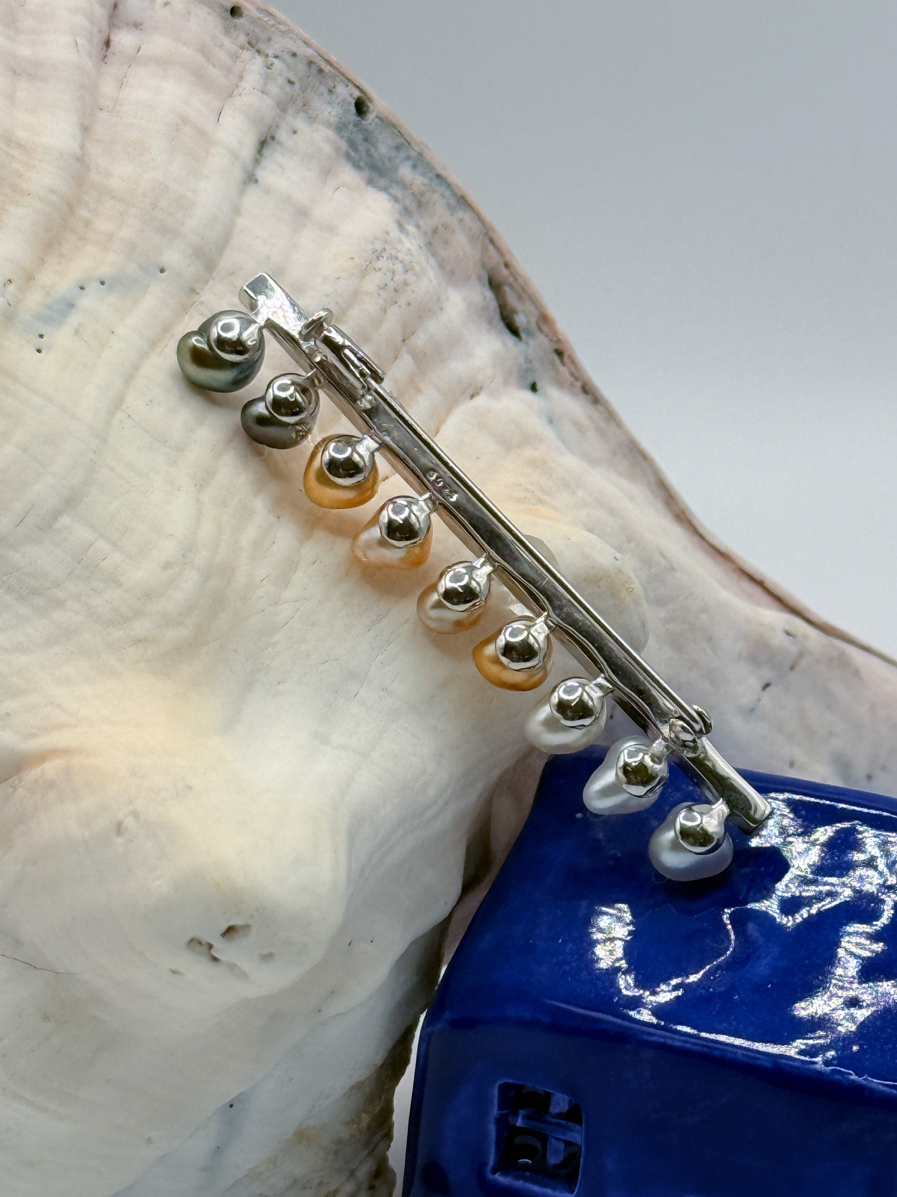 Details of the mount and pin mechanism of the brooch against the conch and blue ceramic house 