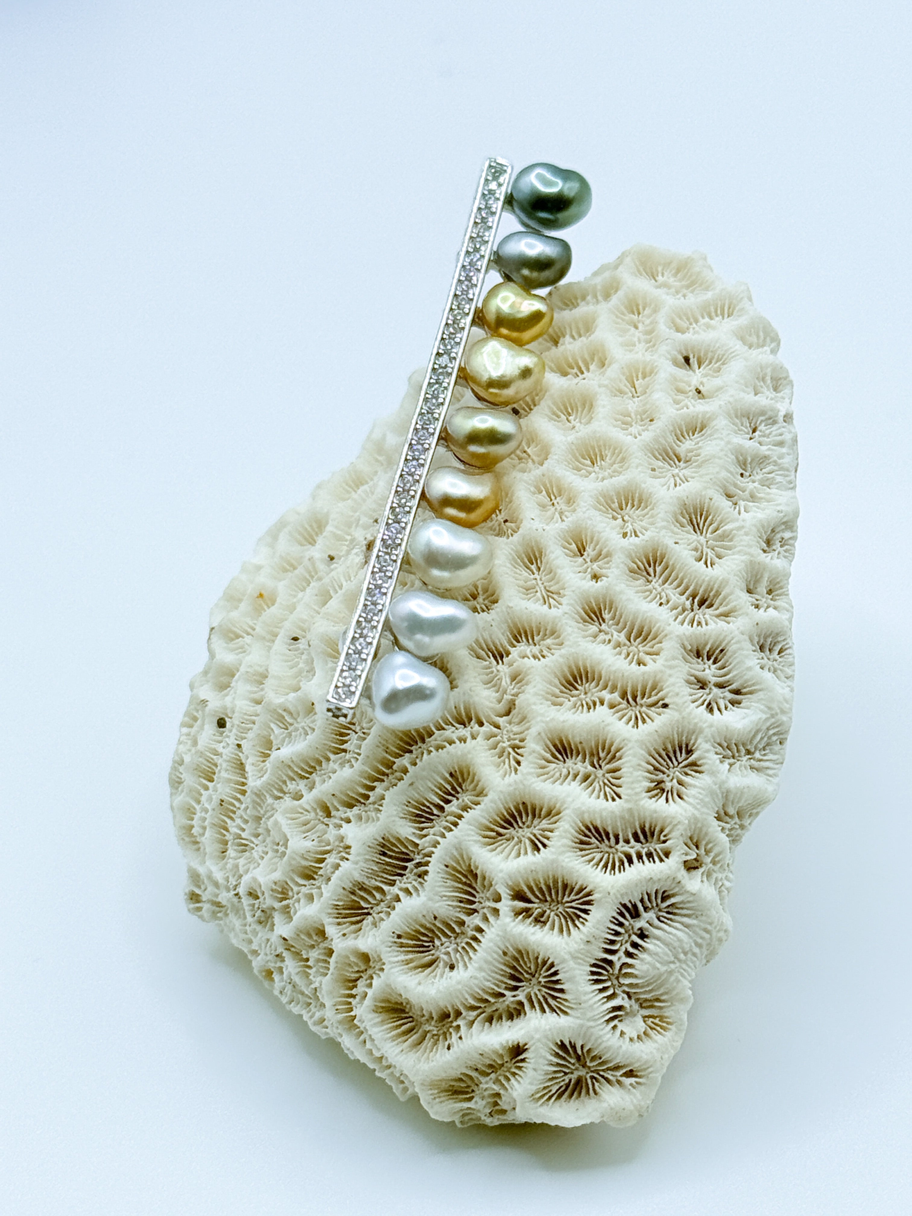 Sterling silver bar pin brooch with multi-coloured heart-shaped keshi pearls displayed on white coral specimen, showing the variety of pearl colours from green to golden to silver