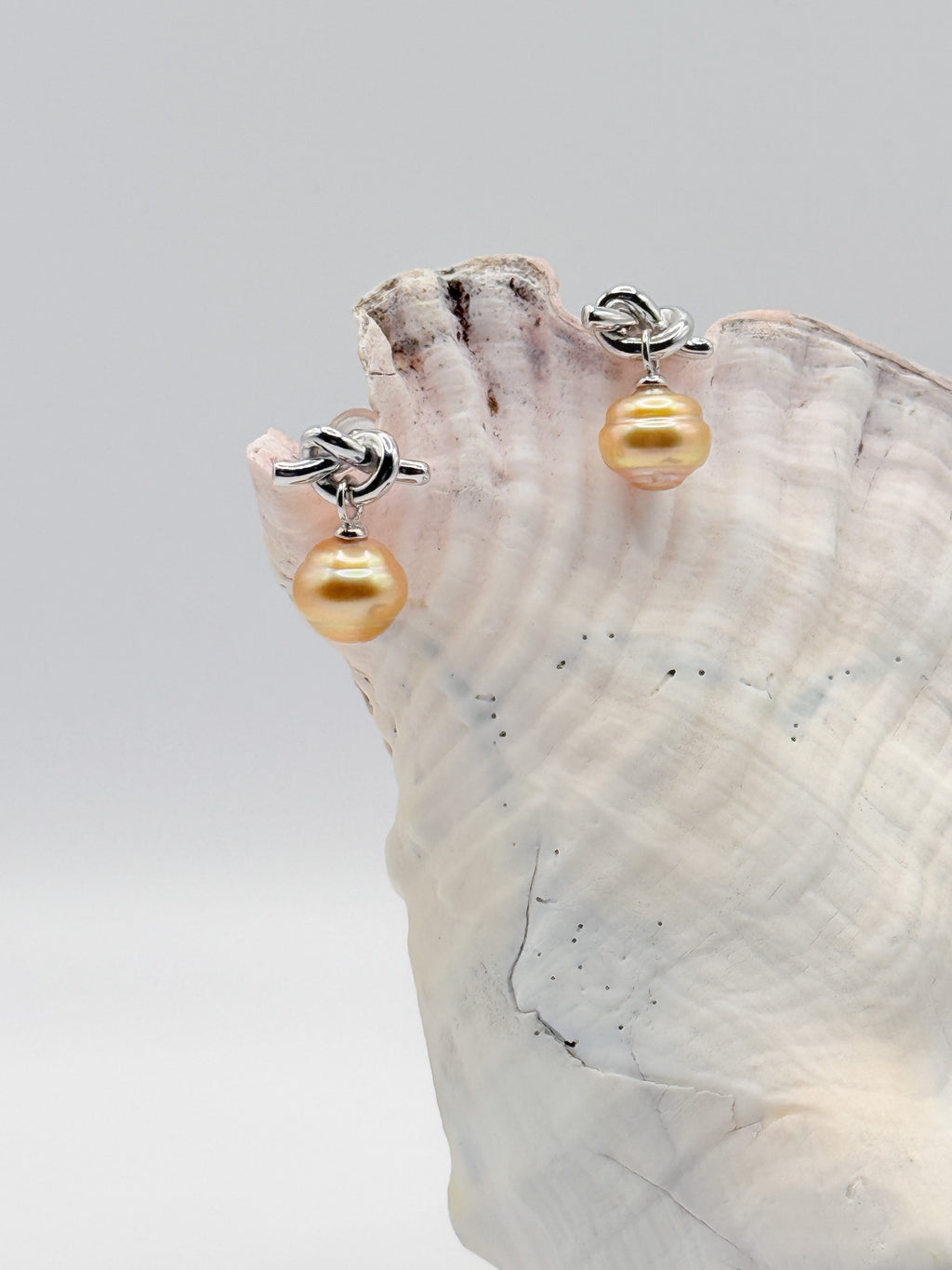Sterling silver earrings with golden South Sea pearls and decorative knot details displayed on pink conch, showing the elegant drop design