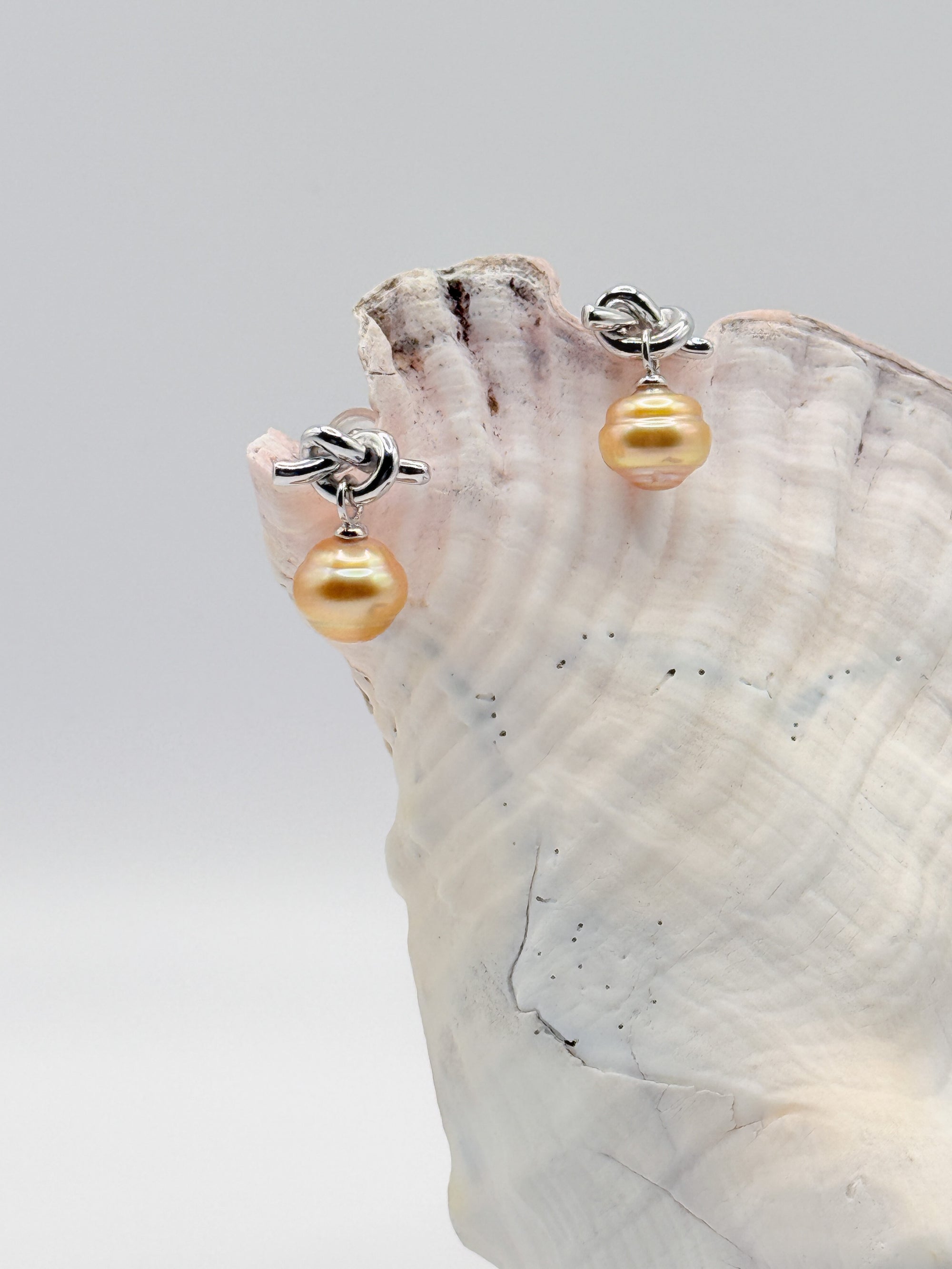 Sterling silver earrings with golden South Sea pearls and decorative knot details displayed on pink conch, showing the elegant drop design