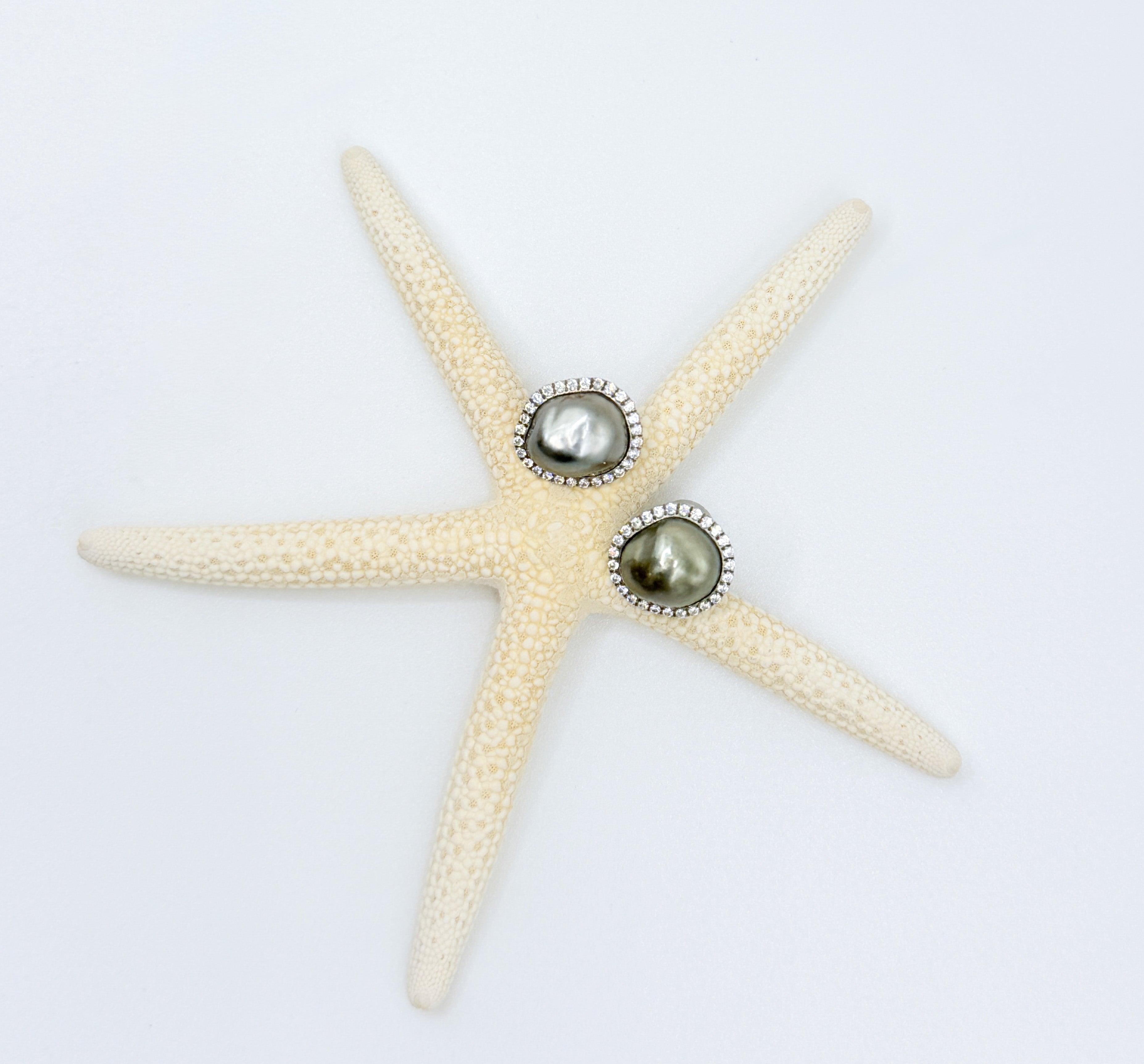 Top-down view of Tahitian Keshi pearl stud earrings on starfish showing CZ pavé halos silver charcoal olive pearl colours