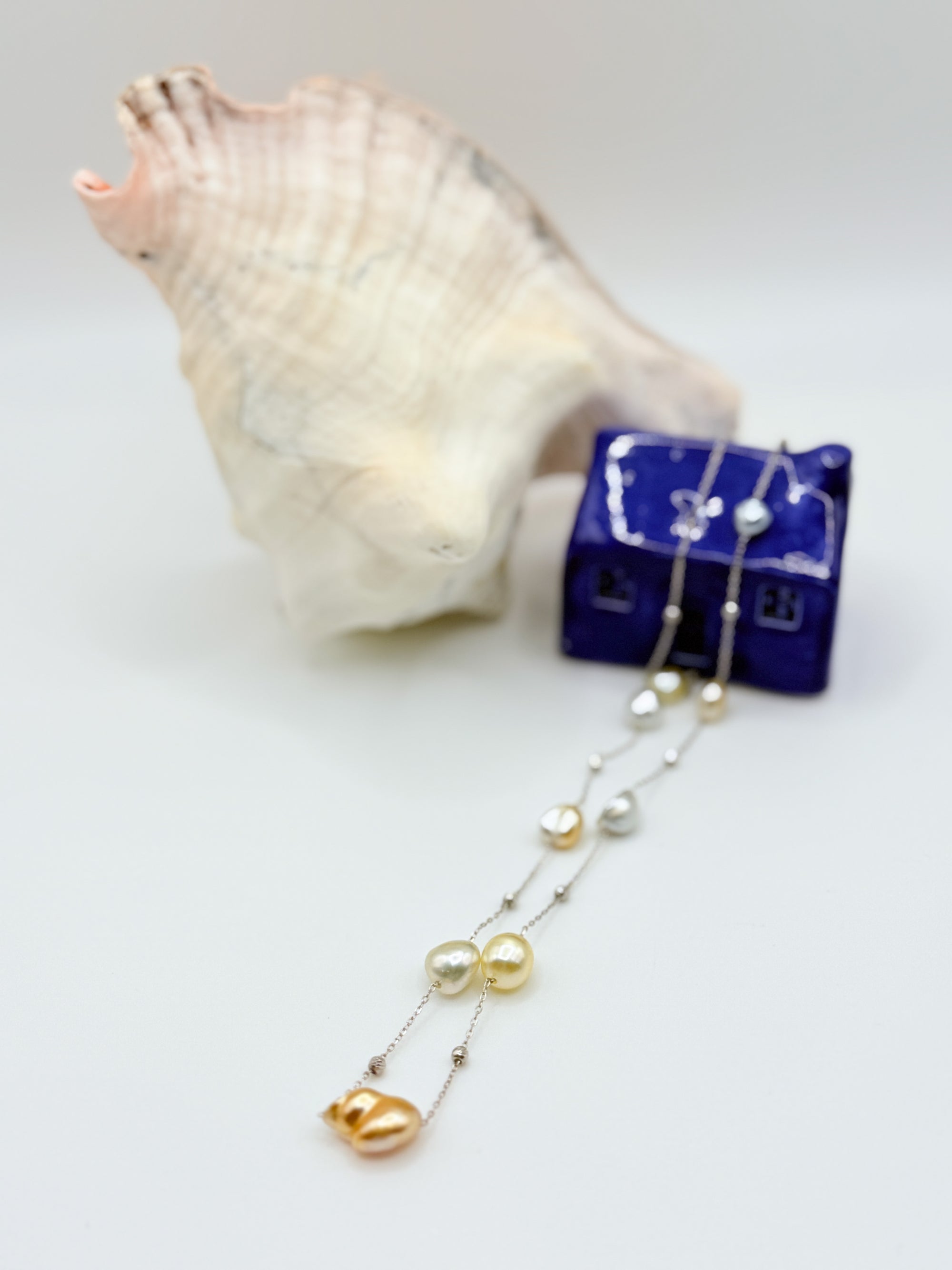 South Sea Keshi pearl station necklace showing gold white pearls 925 sterling silver chain on sea shell styling