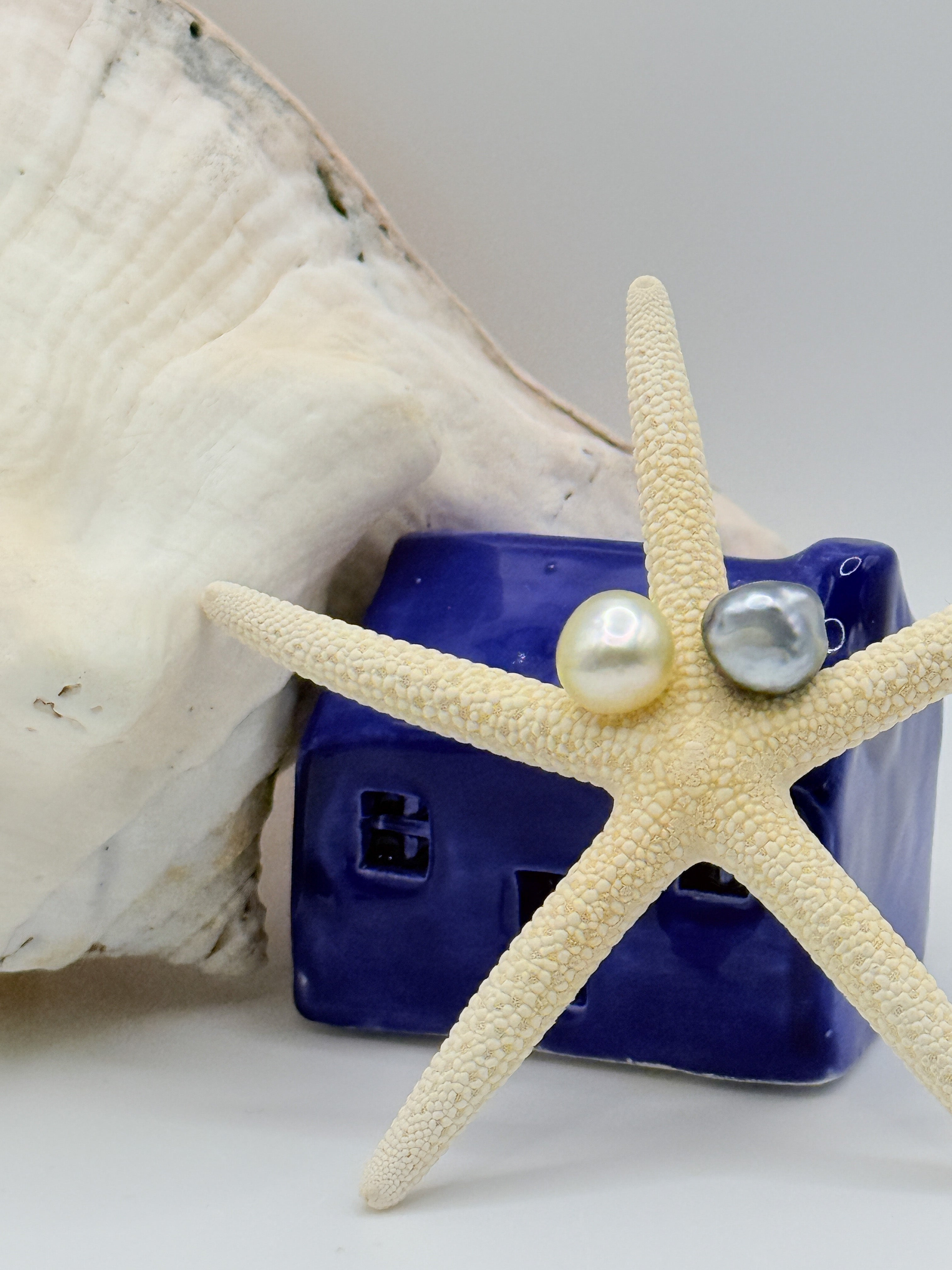 Asymmetrical South Sea Tahitian pearl stud earrings golden and platinum grey pearls over 10mm 925 sterling silver on starfish against a blue house and seashell 