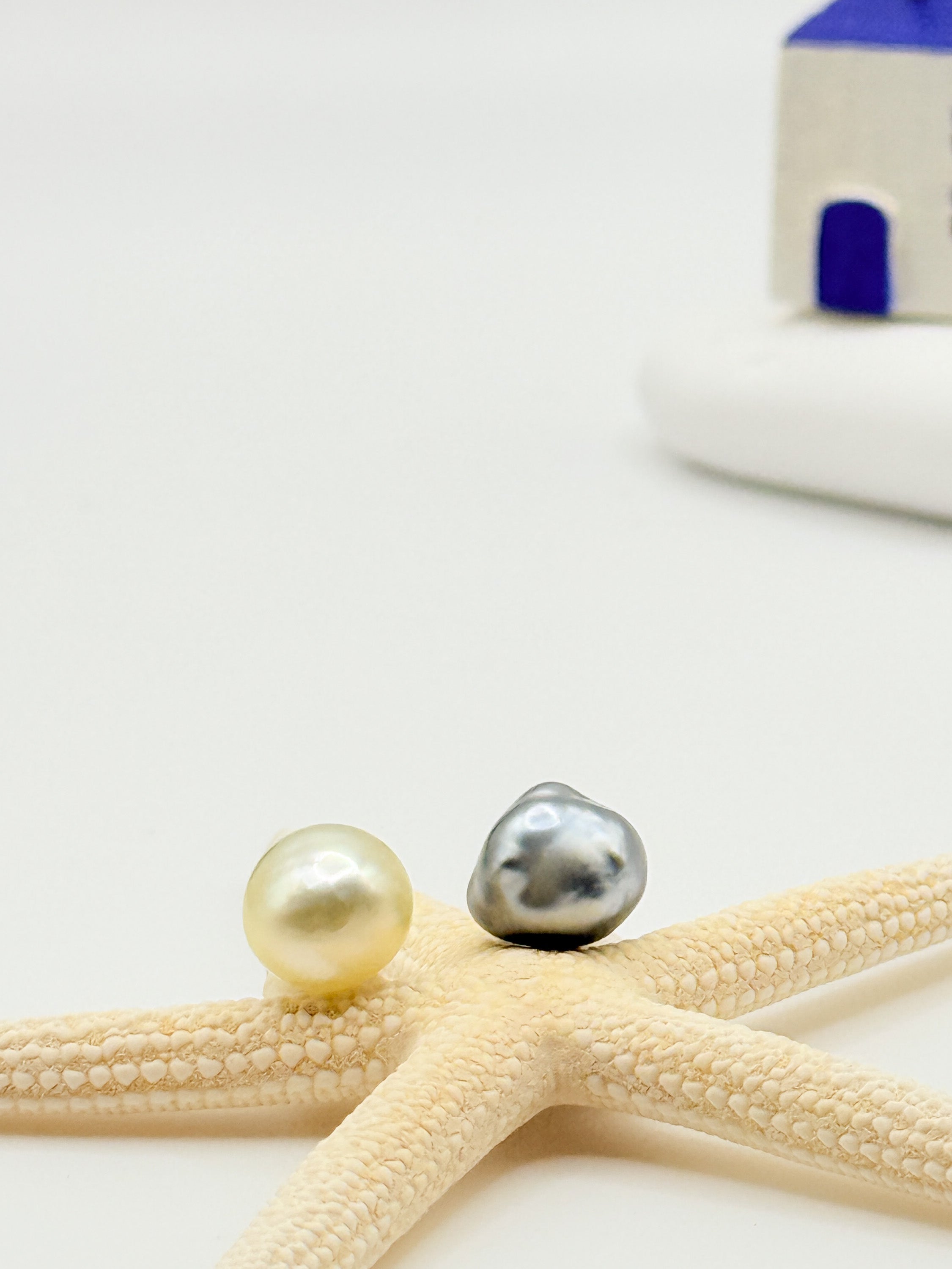 Asymmetrical South Sea Tahitian pearl stud earrings close up showing golden South Sea and platinum grey Tahitian pearls resting on starfish