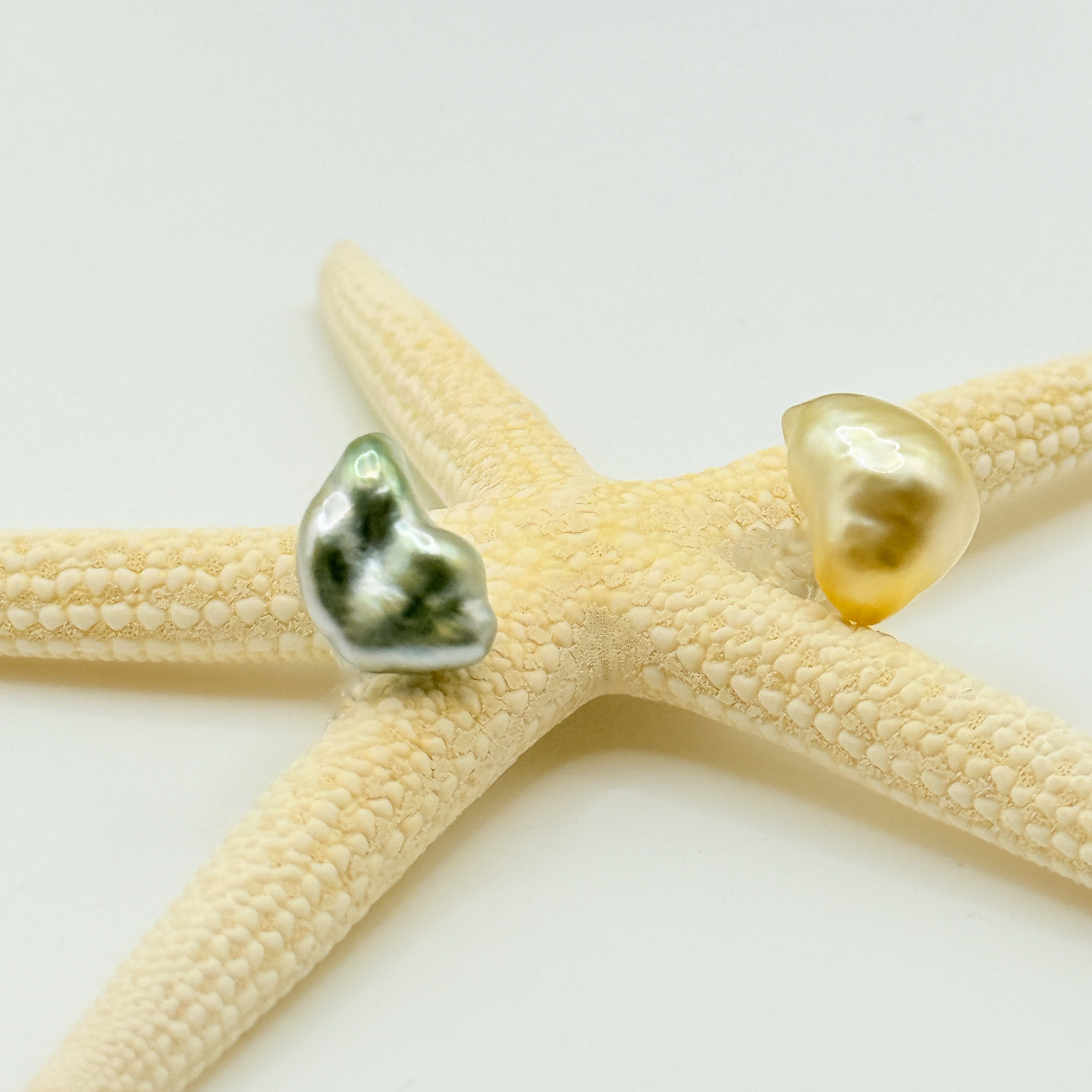 Half-moon Tahitian gold South Sea pearl stud earrings close up showing crescent moon baroque pearls golden and silvery-green tones resting on starfish