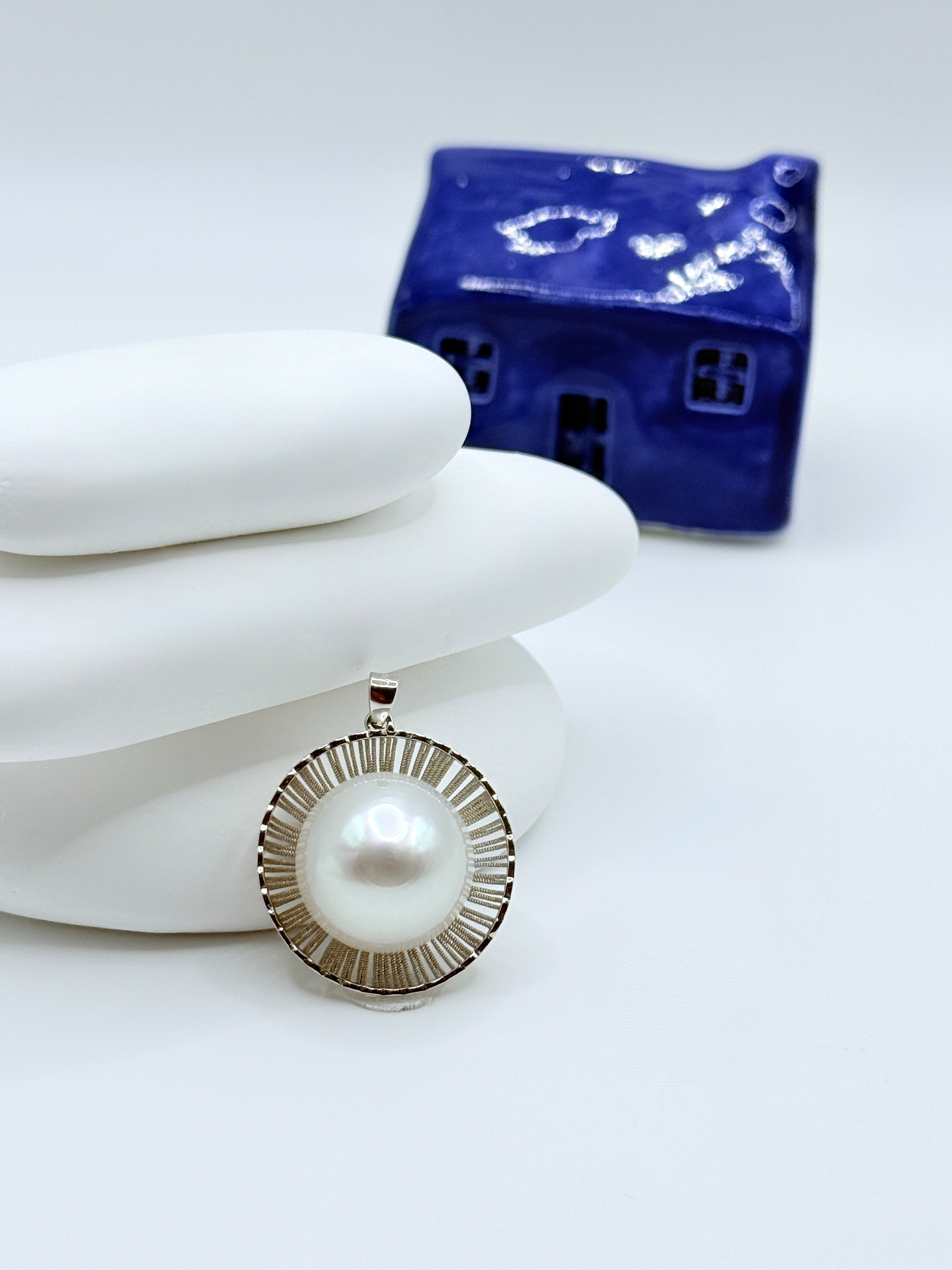 Extra large 15.7mm white South Sea baroque pearl pendant in sterling silver ridged setting displayed on white stones with blue ceramic house