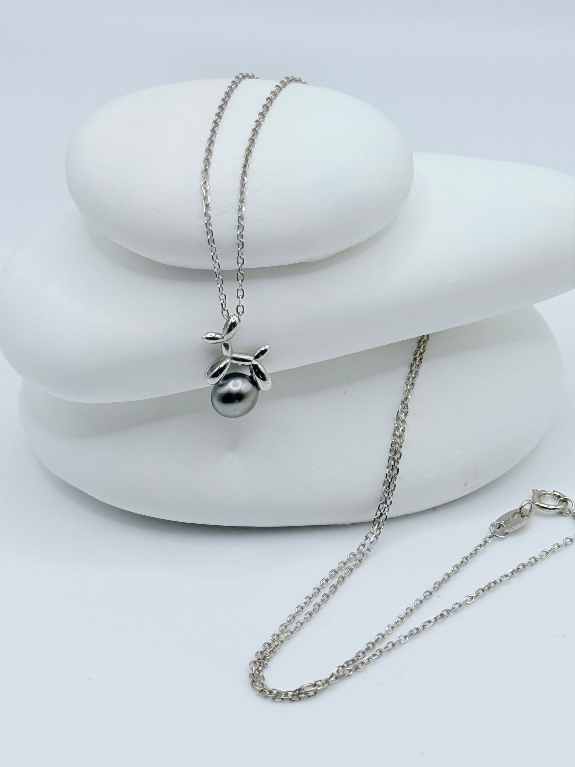 Silver balloon dog pendant with Tahitian keshi pearl displayed on white ceramic jewellery stands showing contemporary design