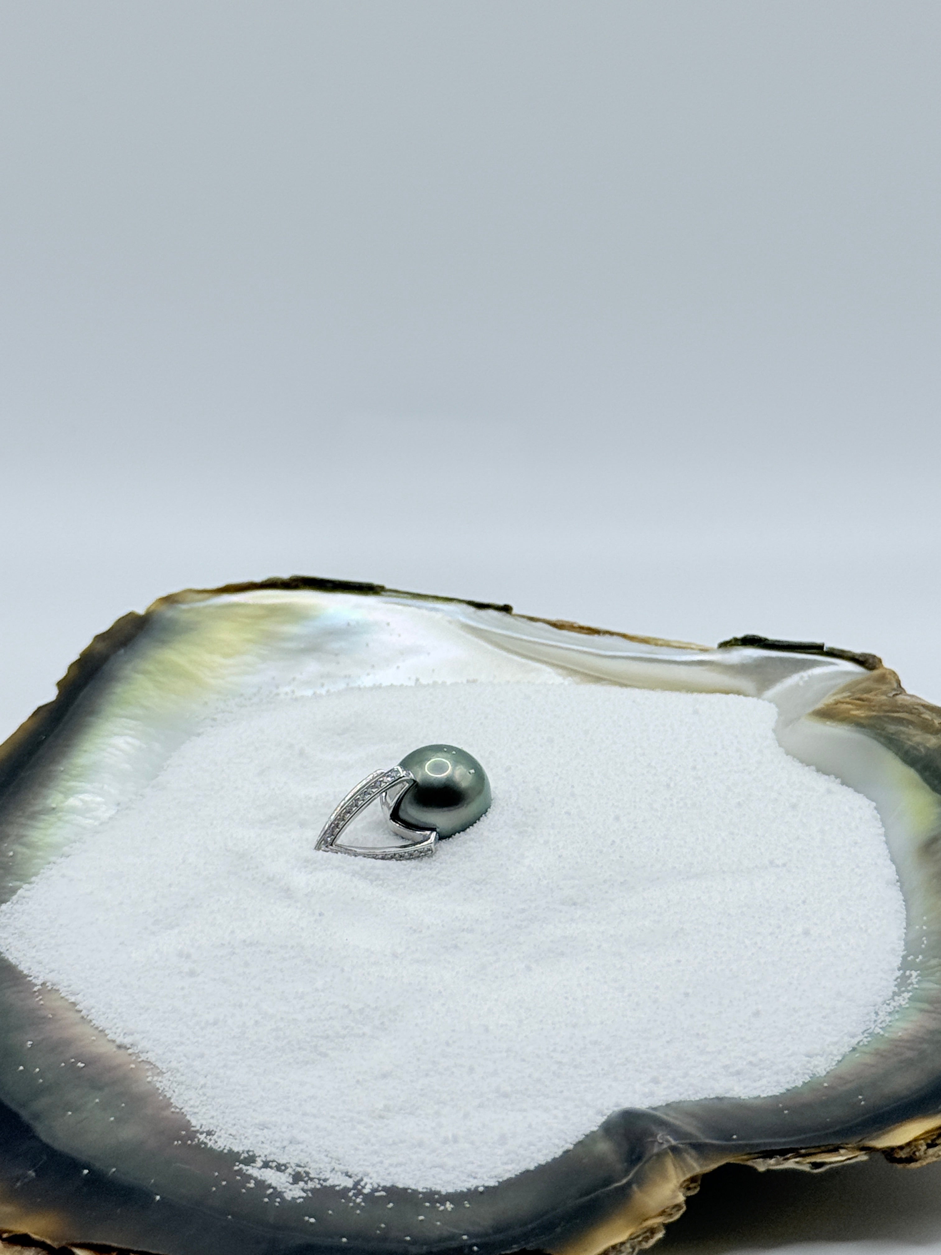 Tahitian pearl pendant with sterling silver bail displayed in oyster shell showing premium quality and natural iridescence