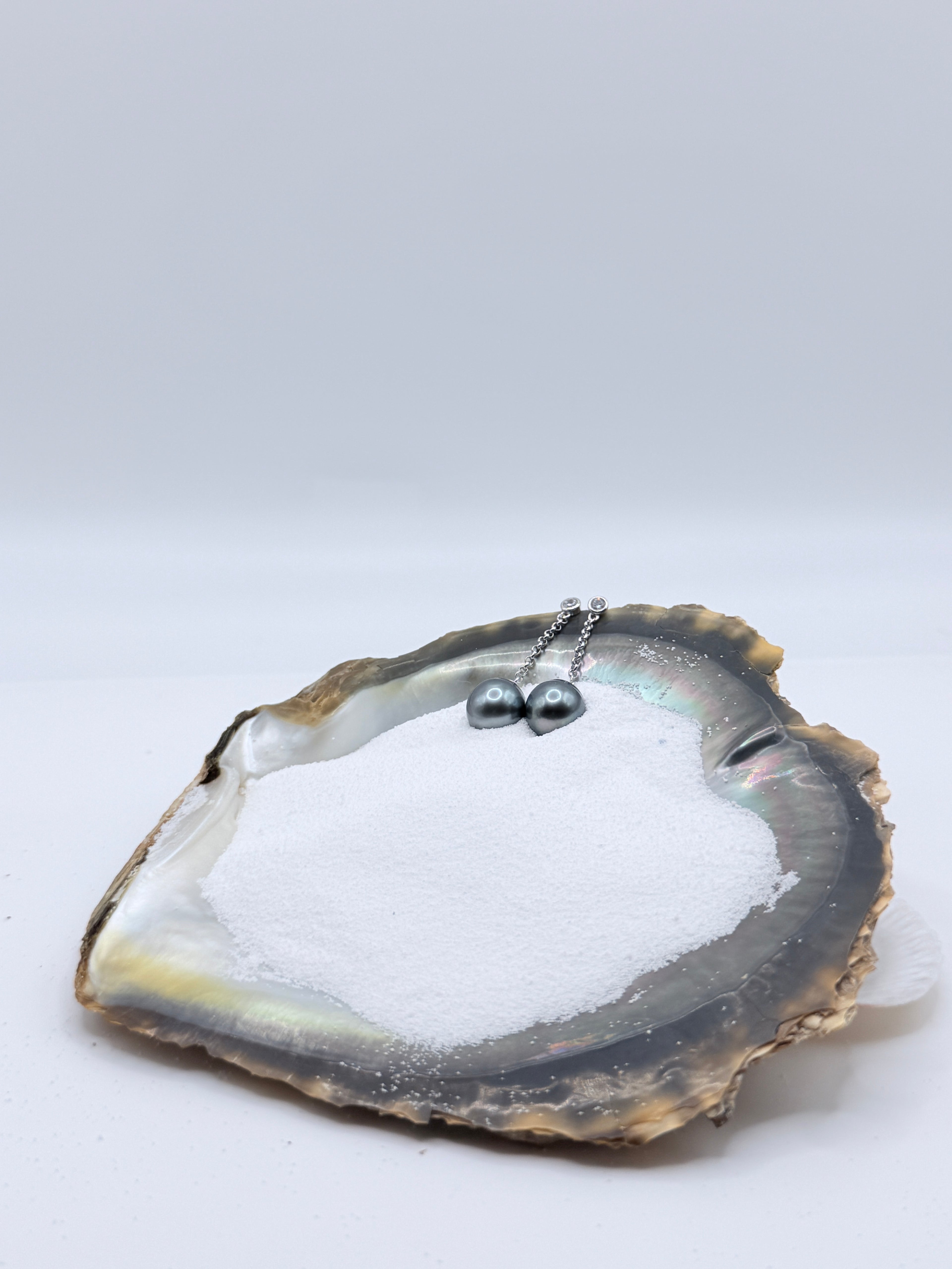 Sterling silver CZ bezel chain earrings with dark grey Tahitian baroque pearls displayed in natural oyster shell showing elegant drop design