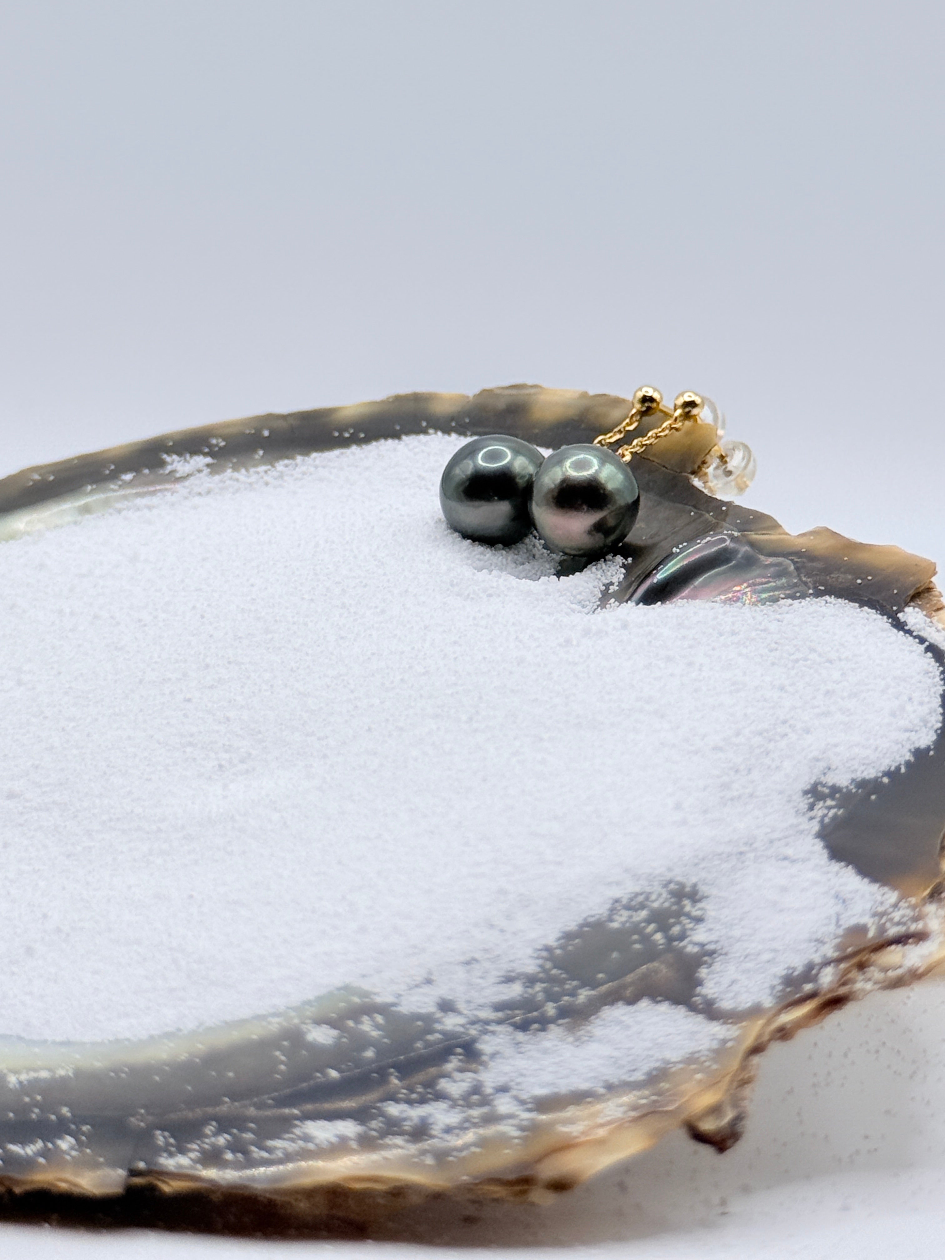 Close-up view of gold plated Tahitian pearl dangle earrings in oyster shell highlighting dark lustre and warm gold chain details