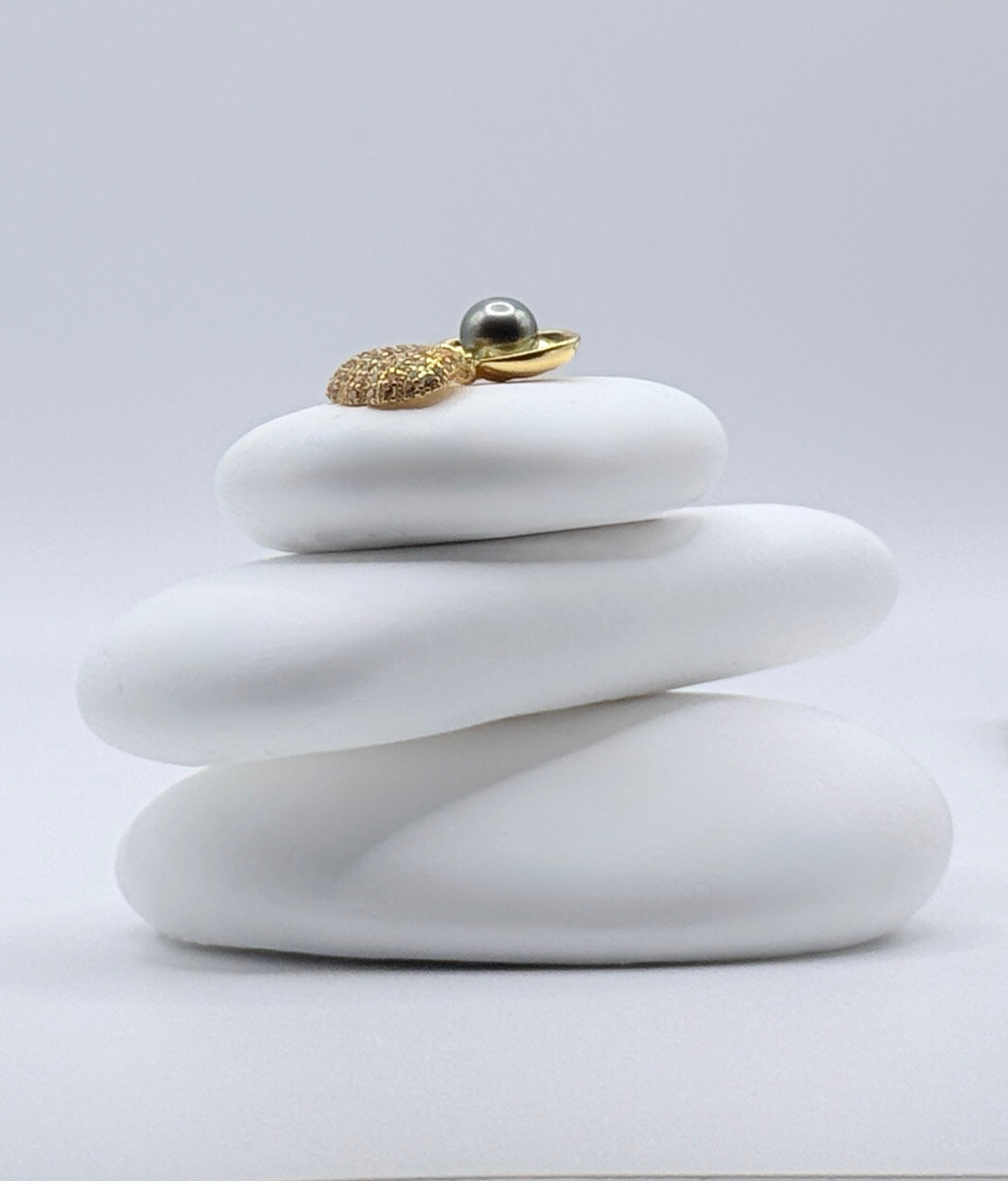 Close-up view of Sea Shell Serenade gold plated textured scallop shell pendant with lustrous 7mm Tahitian keshi pearl on white stone showing peacock overtones