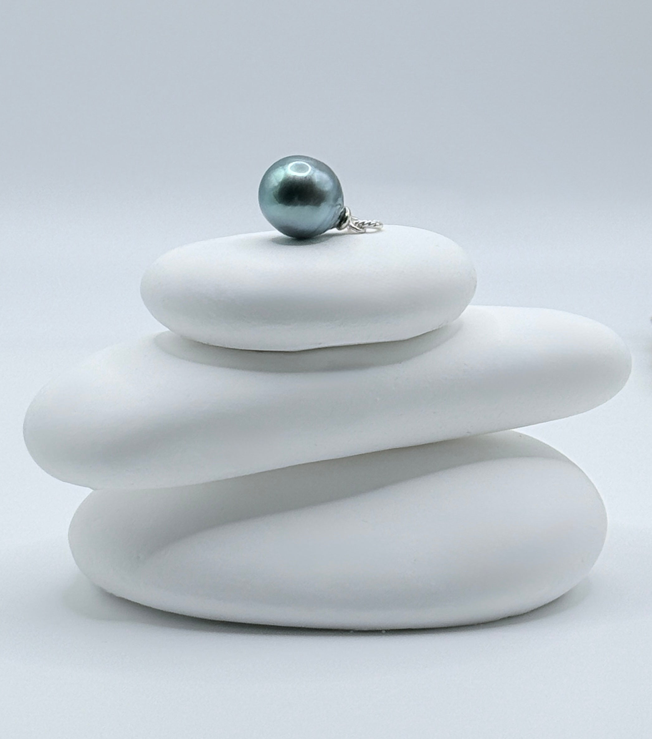 Close-up view of 11x13mm blue Tahitian baroque pearl pendant with sterling silver bail on white stones highlighting teal-blue lustre