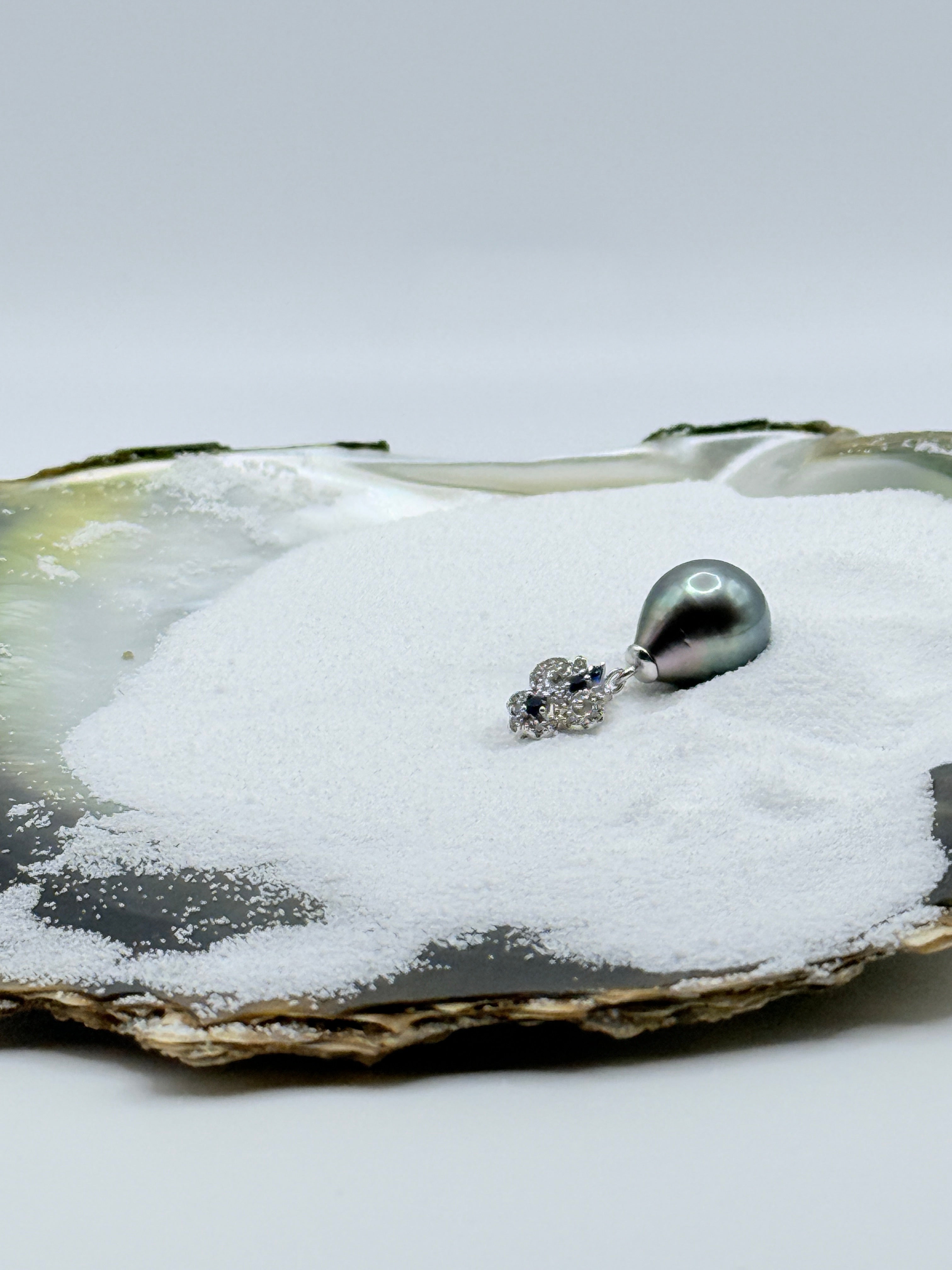 Sterling silver CZ bail green Tahitian teardrop pearl pendant displayed in natural oyster shell showing white and blue crystal accents