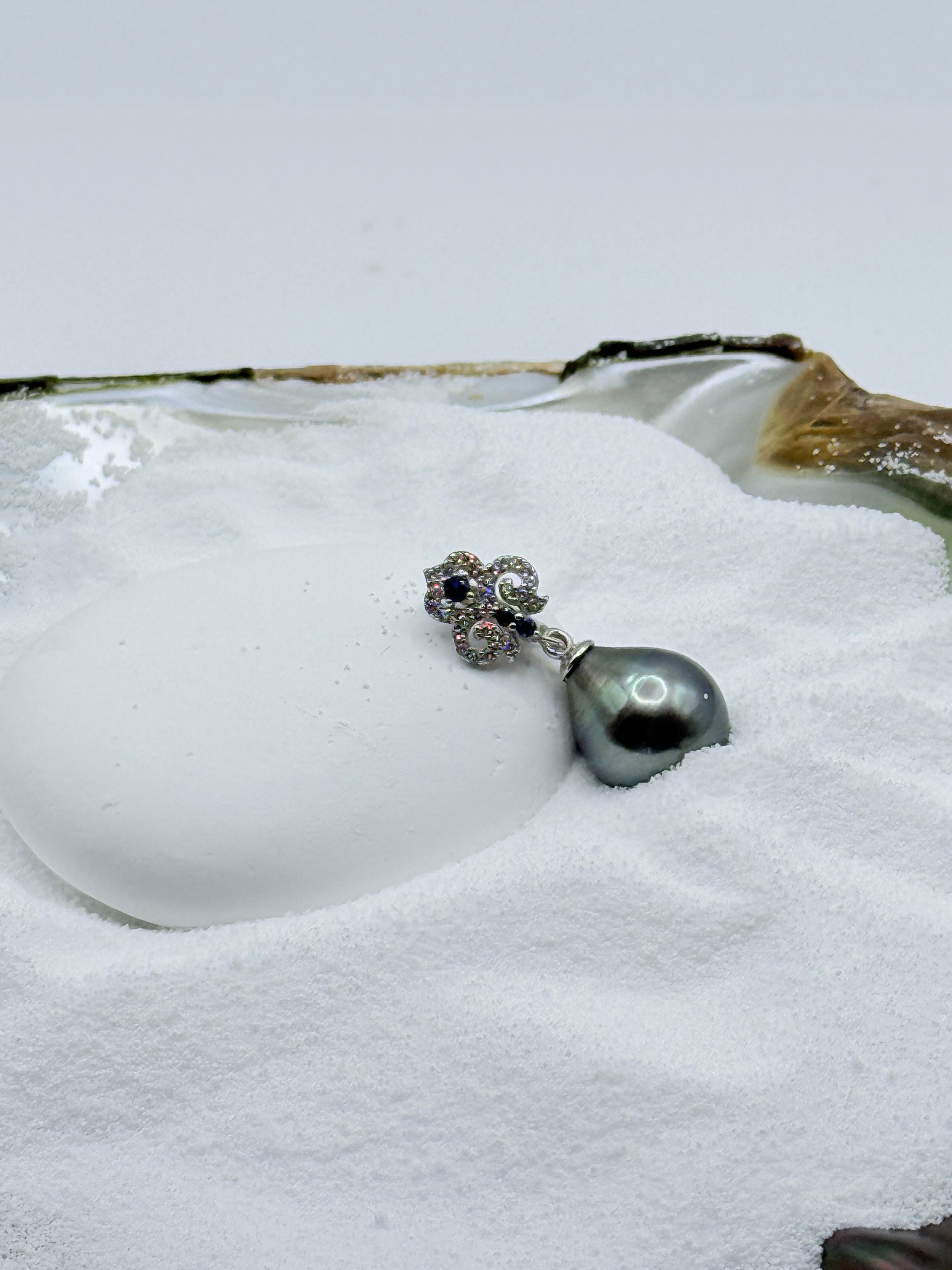 Close-up view of 11x14mm green Tahitian teardrop baroque pearl pendant with sterling silver bail set with white and blue CZ stones in oyster shell