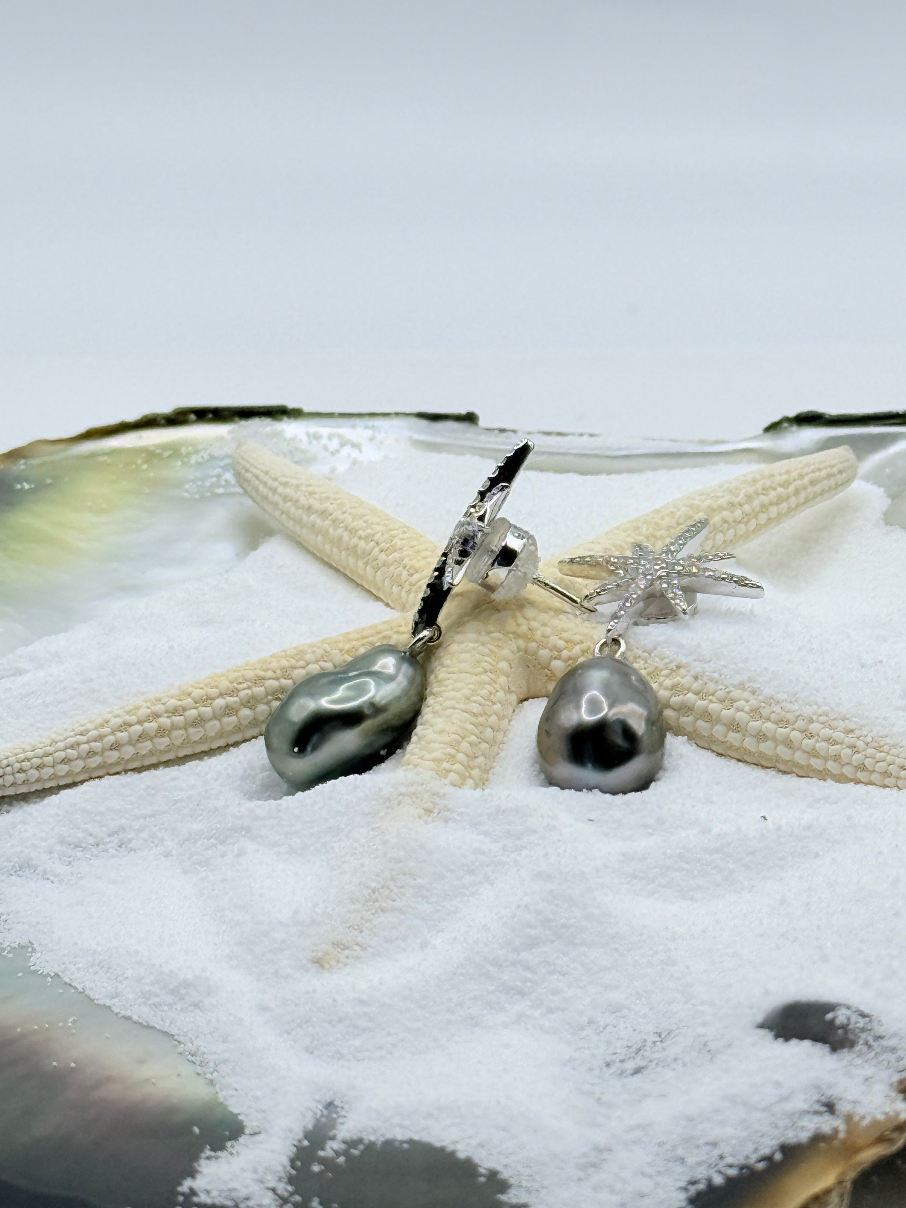 View of pushback closure of stellar Dance sterling silver CZ star drop earrings with charcoal grey Tahitian keshi pearls displayed in natural oyster shell and starfish styling