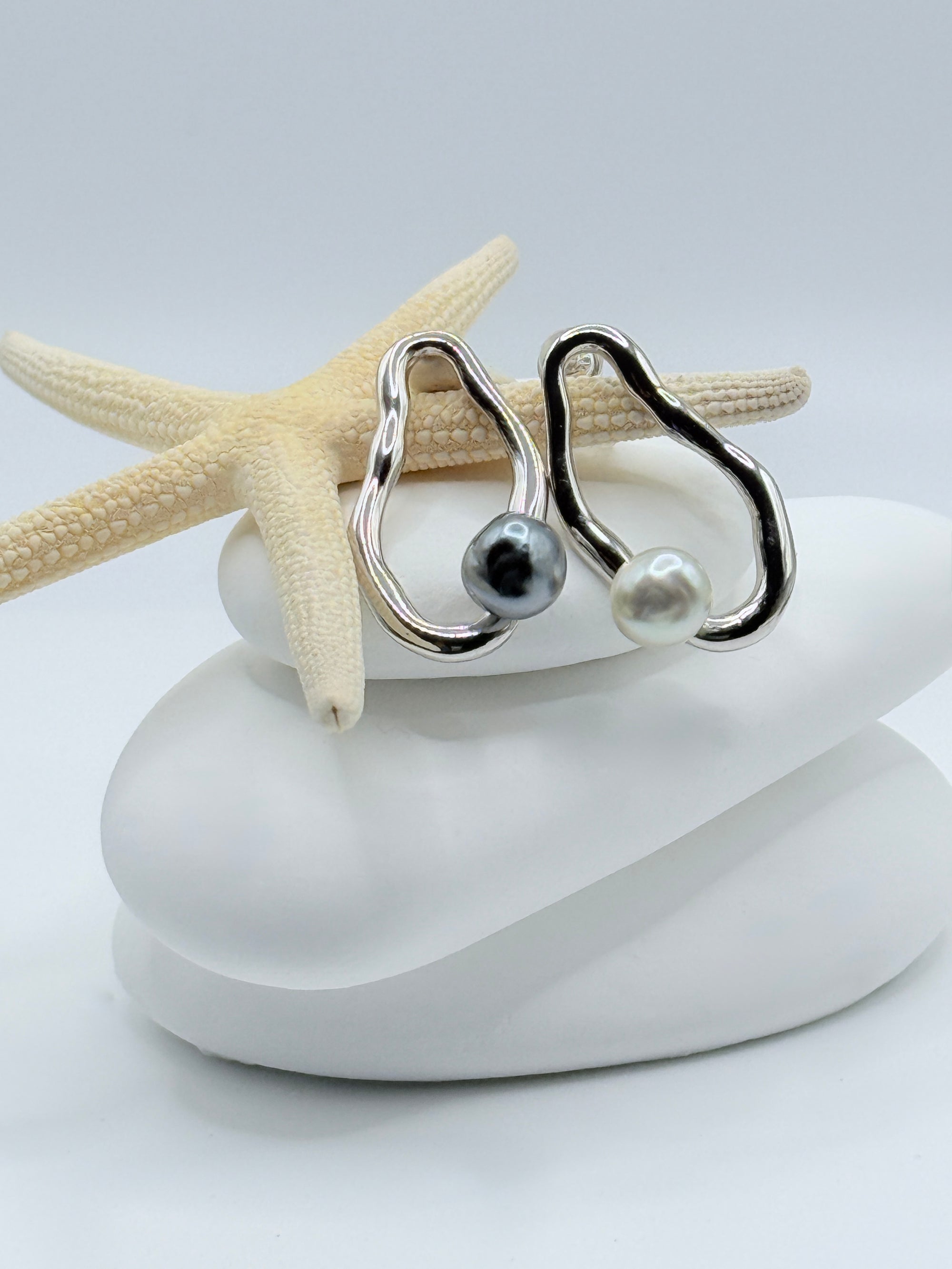 Pebble sterling silver asymmetric earrings with blue-grey Tahitian keshi and white South Sea keshi pearls displayed on white stones with starfish
